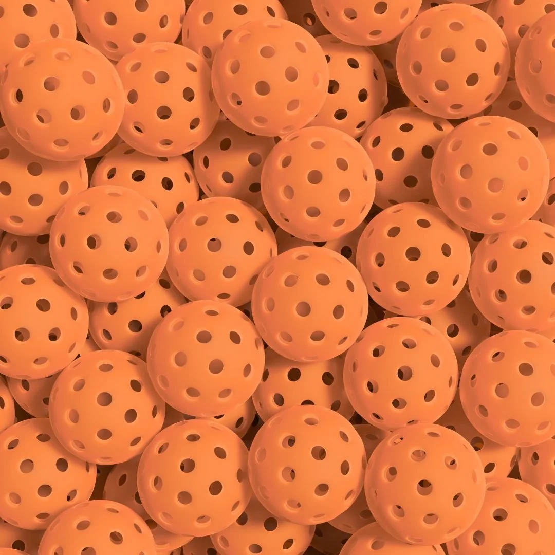A photo of dozens of orange pickleballs on top of each other.