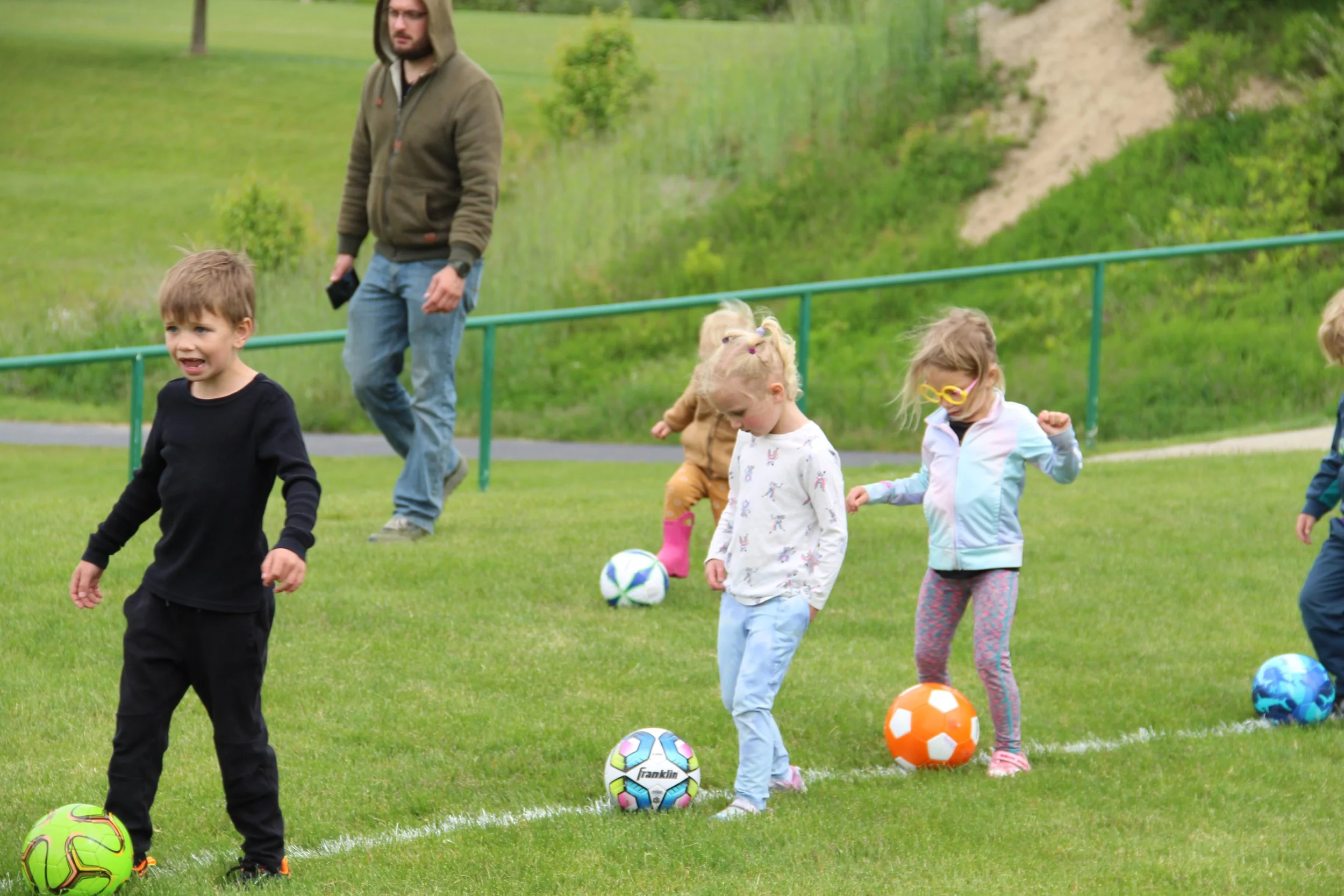A group of kids kick colorful soccer balls around a soccer field.