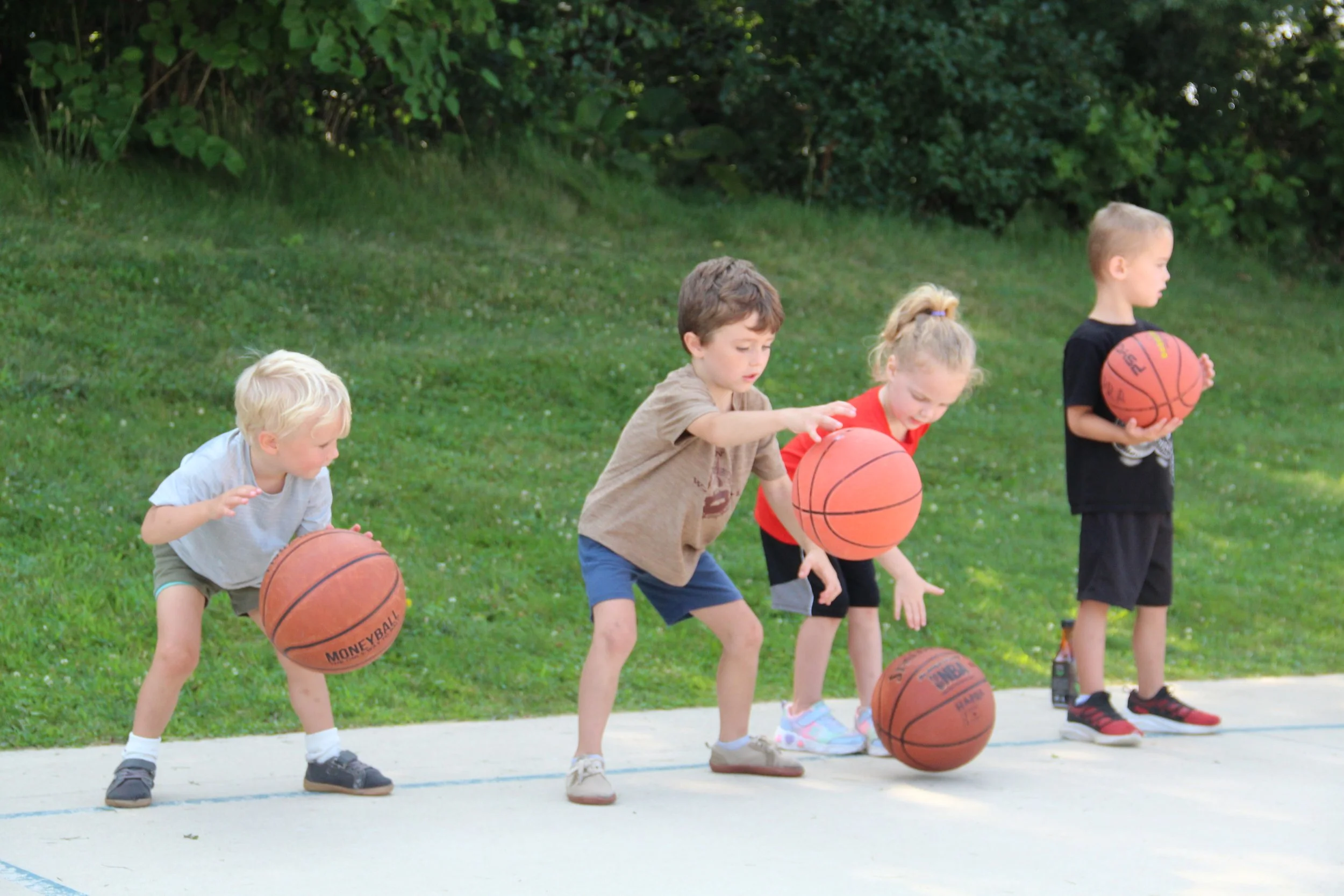 Four kids dribble basketballs on an outdoor court.