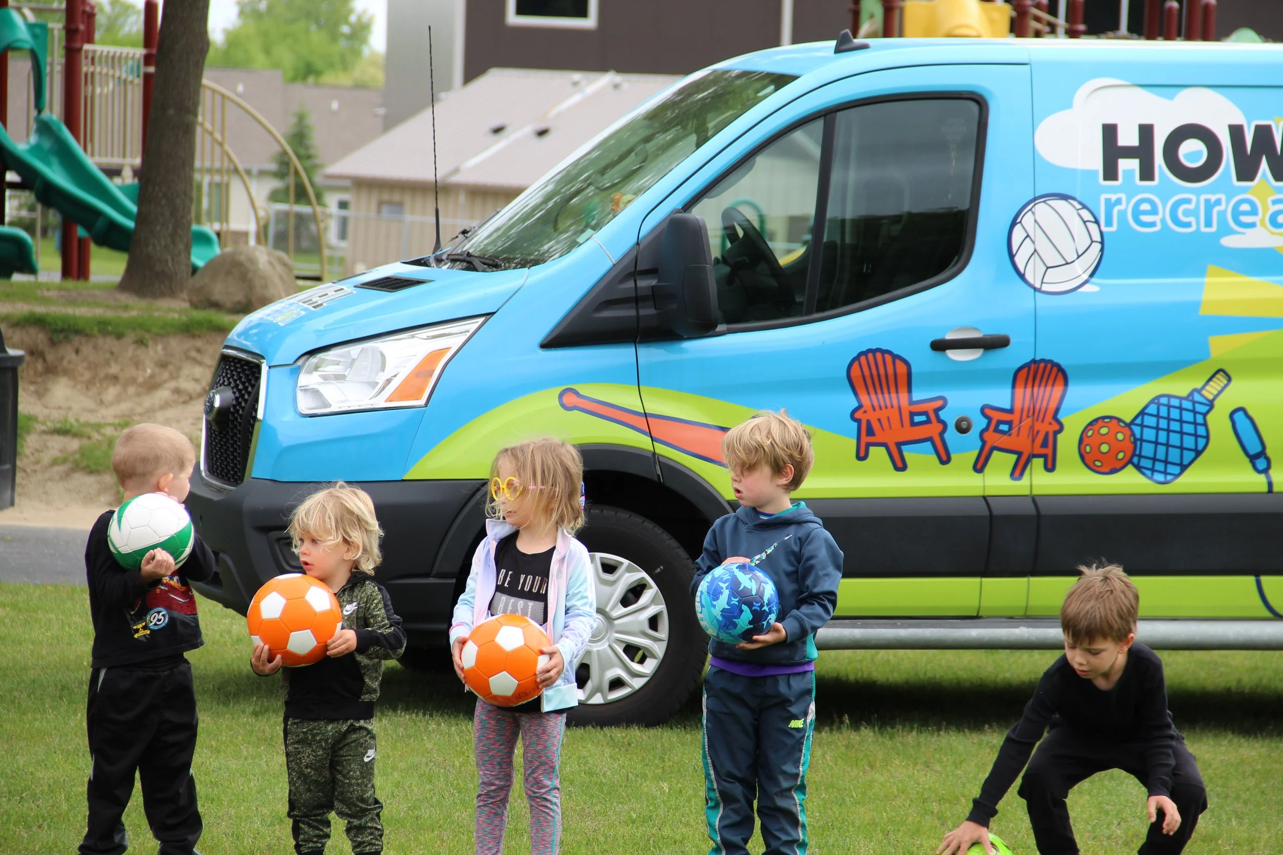 Four kids hold soccer balls in front of the Rec on the Go van.