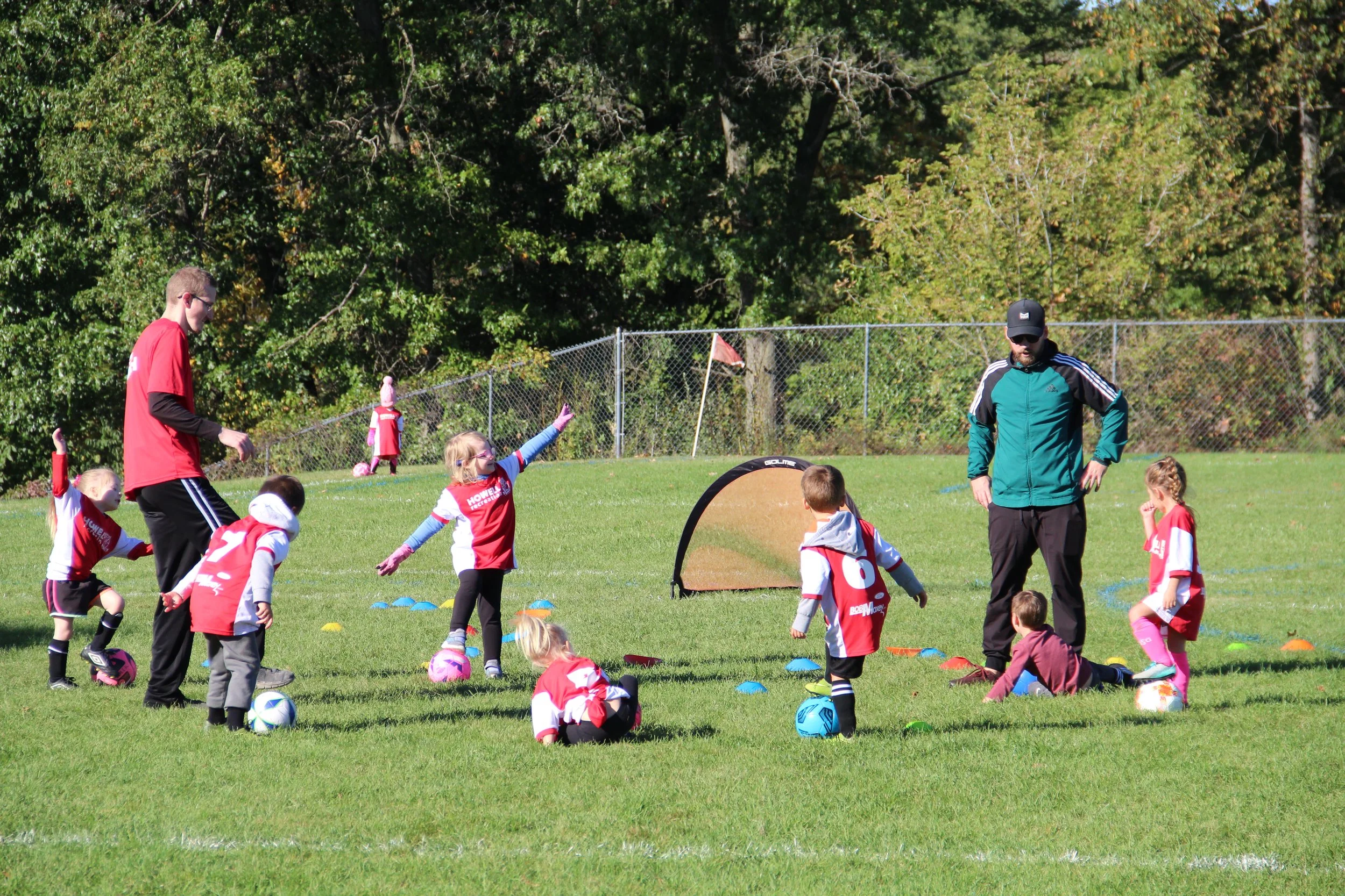 A group of kindergarteners practice kicking a soccer ball into a net.