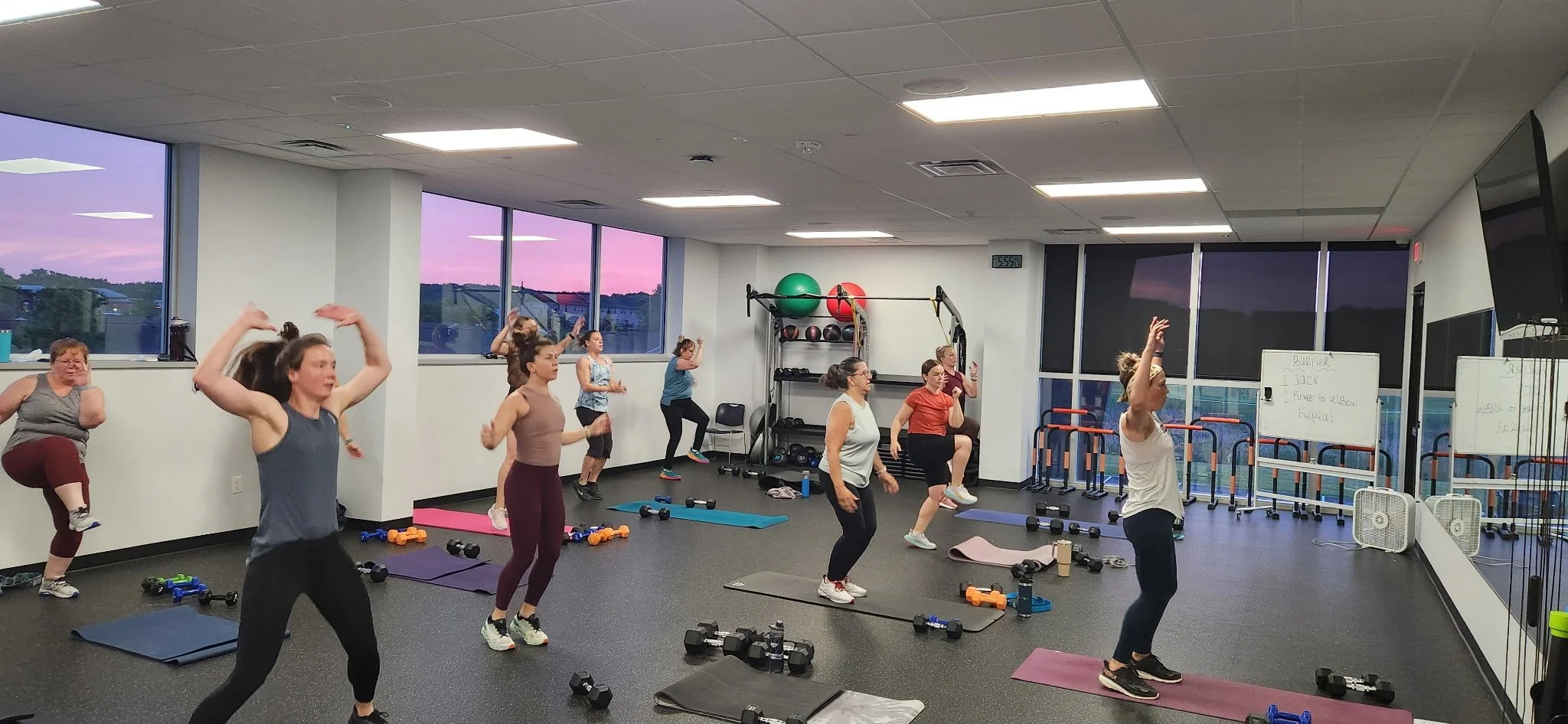 A group of people do jumping jacks while standing on yoga mats in a early morning fitness class.