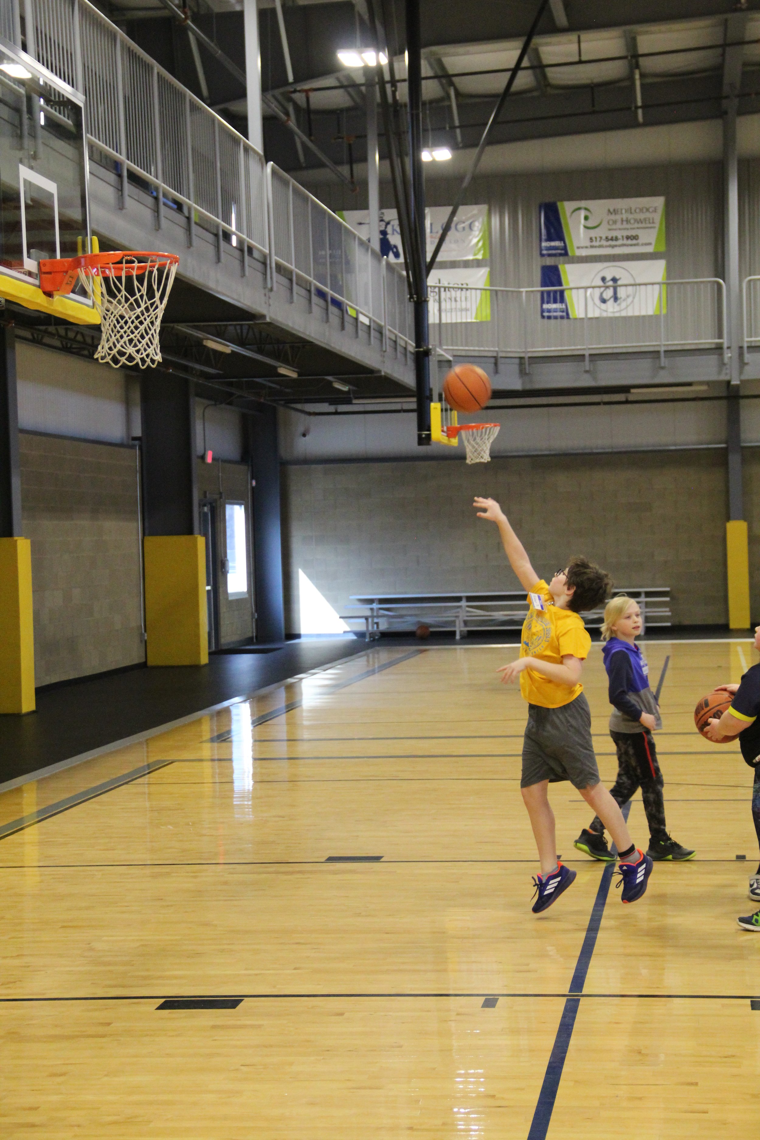 A boy in a yellow shirt shoots a basketball towards the hoop.