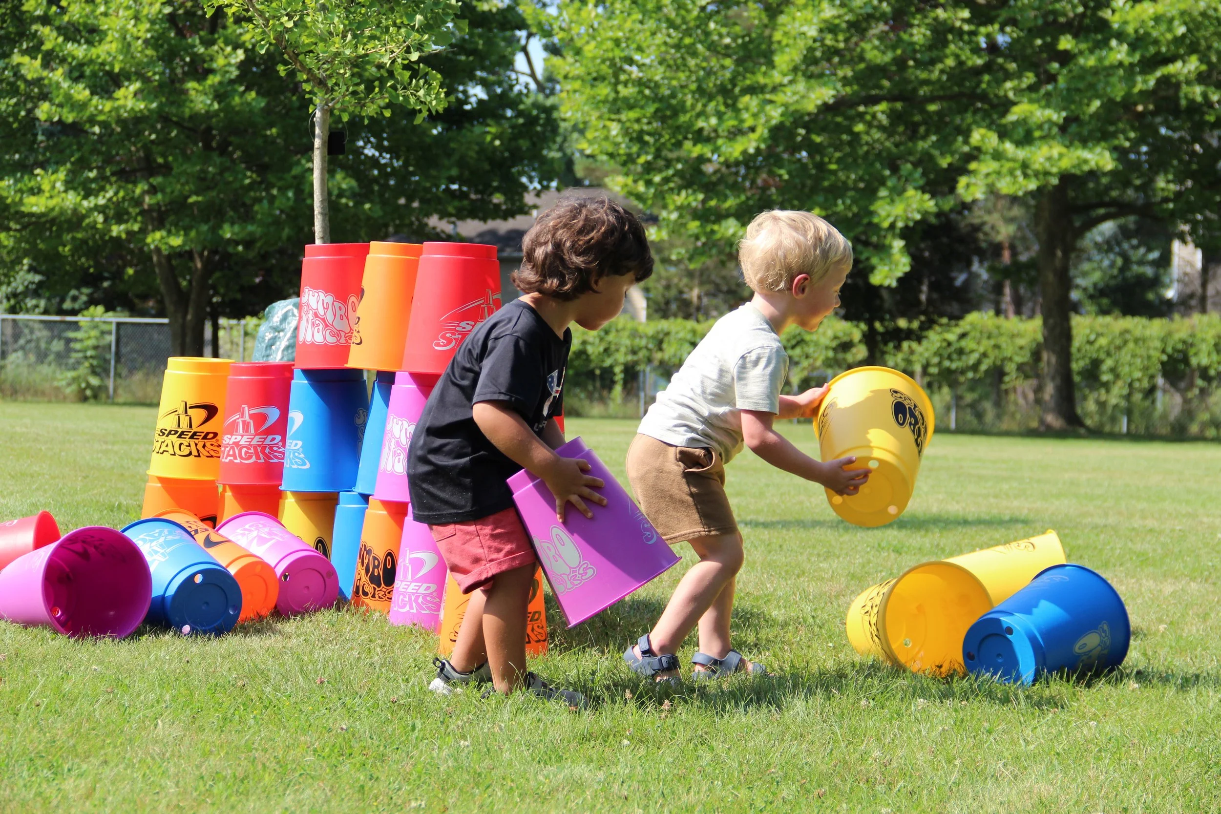Two children play with giant, colorful stacking cups outside at a park.
