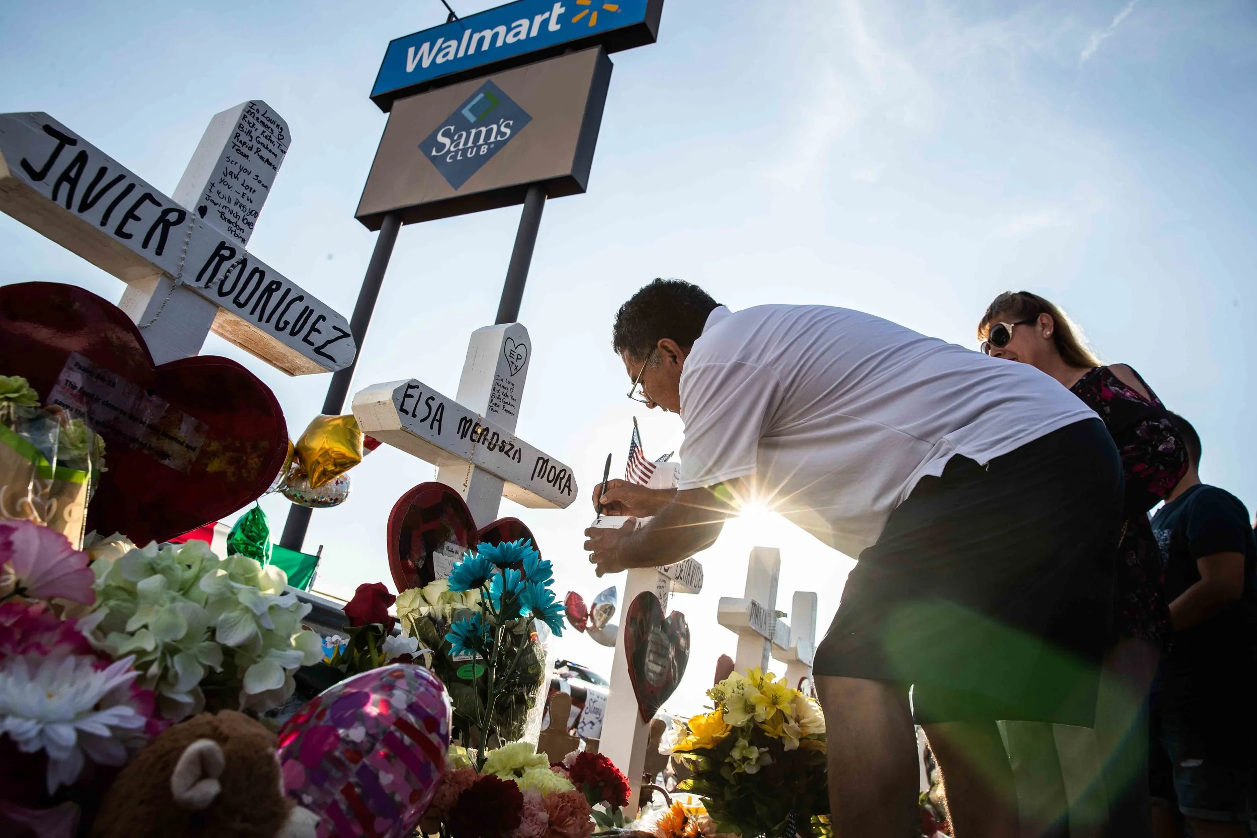 Armando Moreno next to his wife Martha Moreno, writes a message on Arturo Benavides' cross to honor his memory in El Paso on Monday, August 5, 2019.