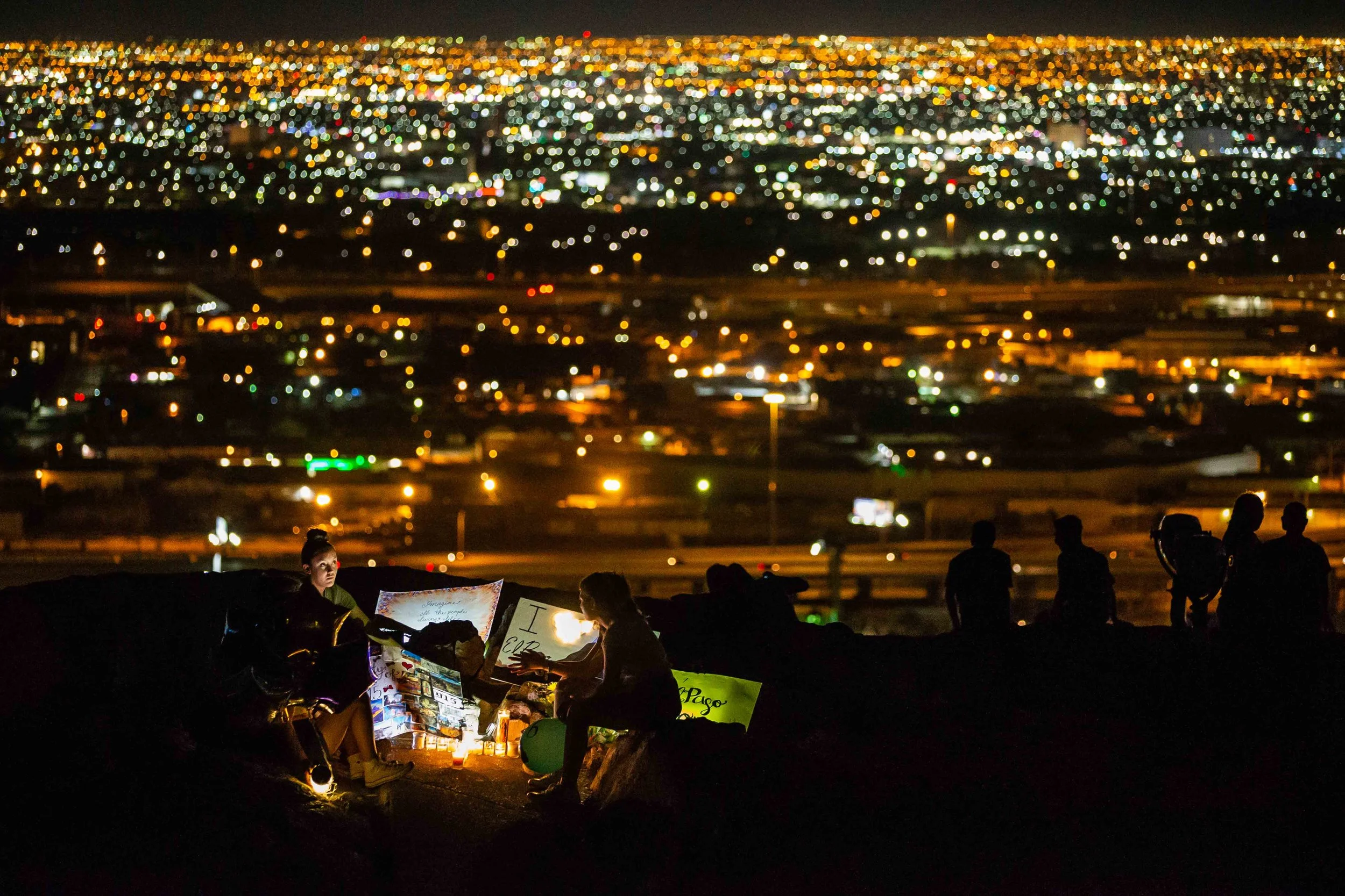 A group of students from Loretto Academy sit next to some posters and candles that were placed at the Scenic Drive - Overlook to honor the victims of the mass shooting occurred in Walmart last Saturday monirng in El Paso on Monday, August 5, 2019.