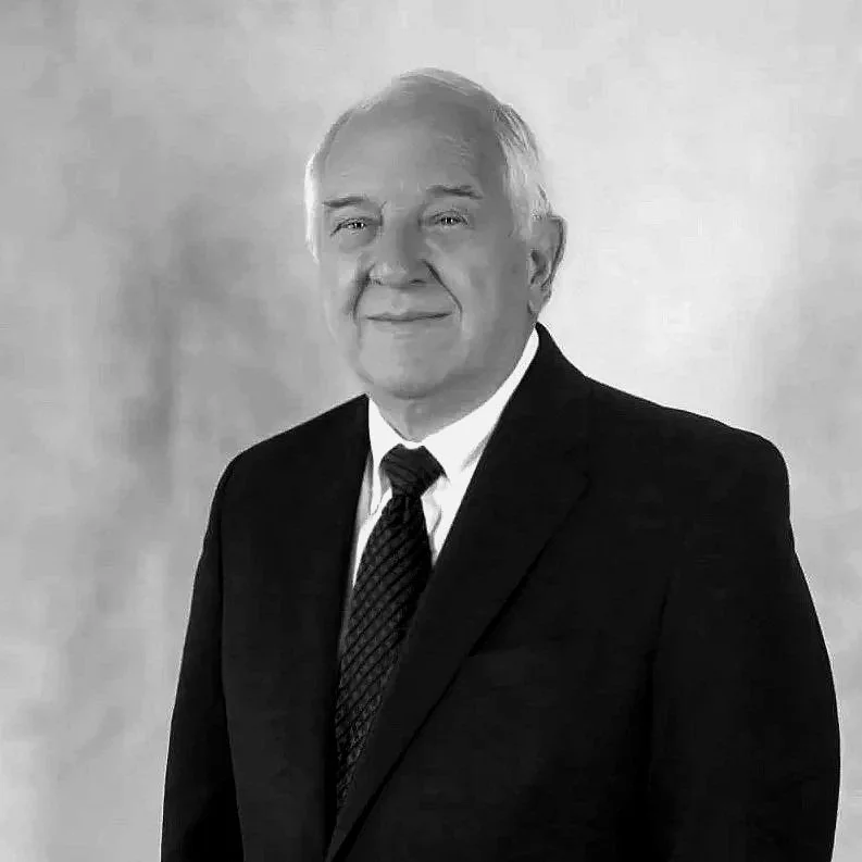 Black and white portrait of an elderly man in a suit and tie, smiling at the camera.