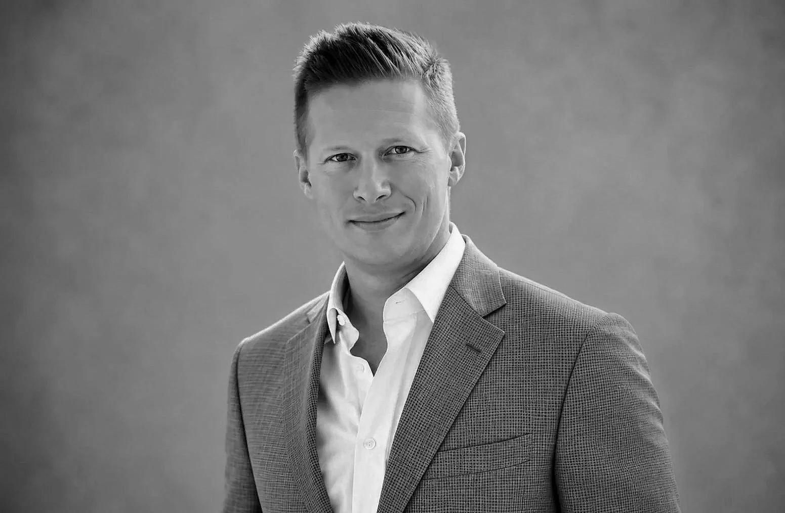Black and white portrait of a man in a suit smiling at the camera.