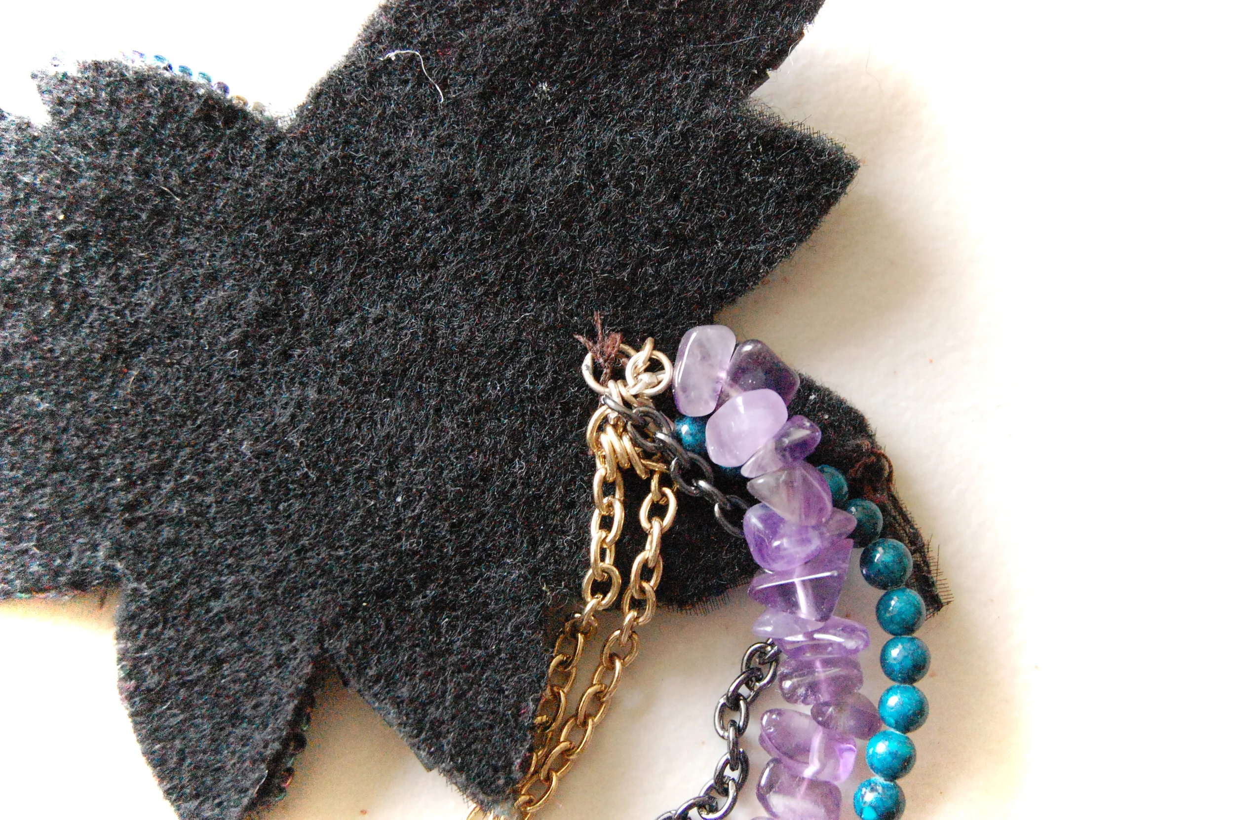 Close up of back of applique piece: beaded strands and chains attached. to sewed-on jump ring. 