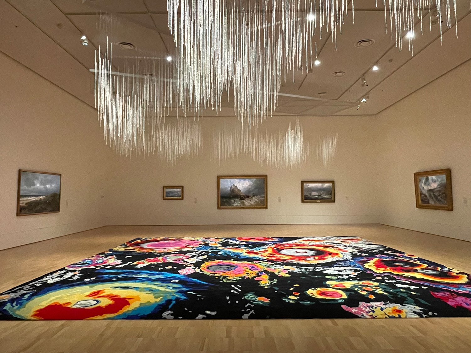   Liquid Skies / Gyrwynt,  2023, wool, textile, 850 x 850 cm  Haku , 2023, glass beads, nylon, metall, 3200 threads, variable dimensions  The installation consists of two works: Liquid Skies / Gyrwynt, a carpet on the floor and Haku, 3200 strings of 