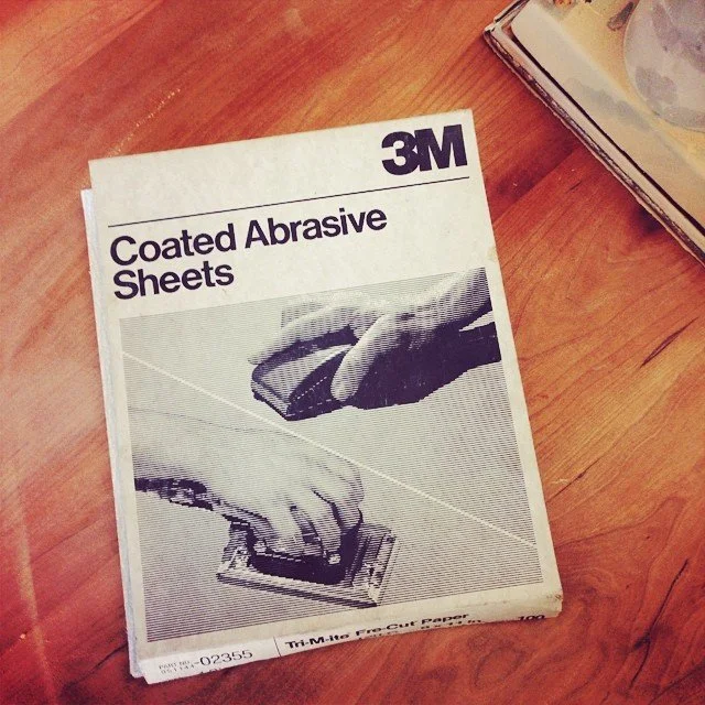 Box of 3M coated abrasive sheets on a wooden surface.