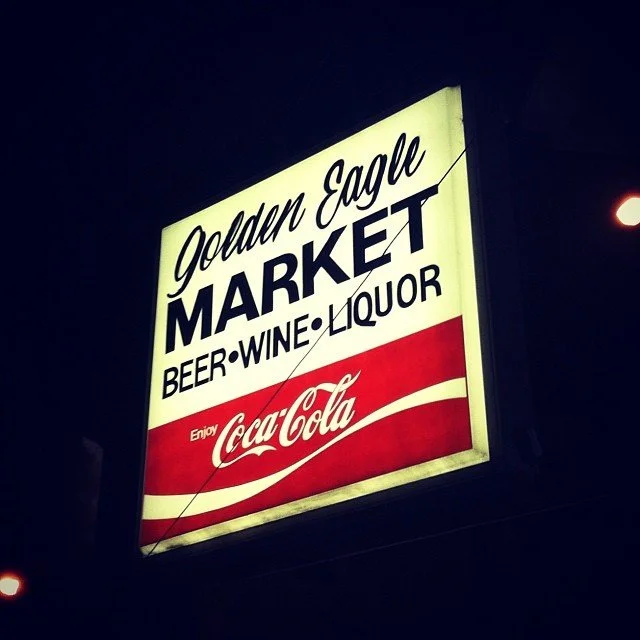 Illuminated sign for Golden Eagle Market offering beer, wine, and liquor, with a Coca-Cola logo at the bottom.