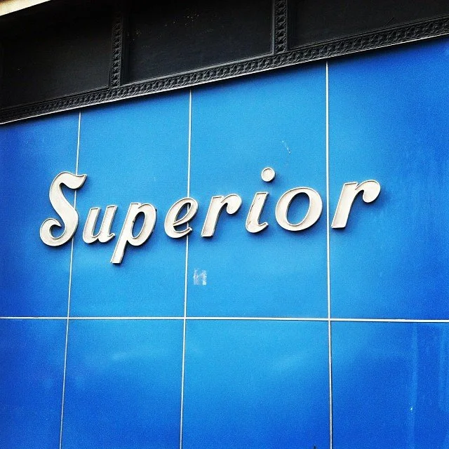 Sign with the word 'Superior' mounted on a blue tiled wall.