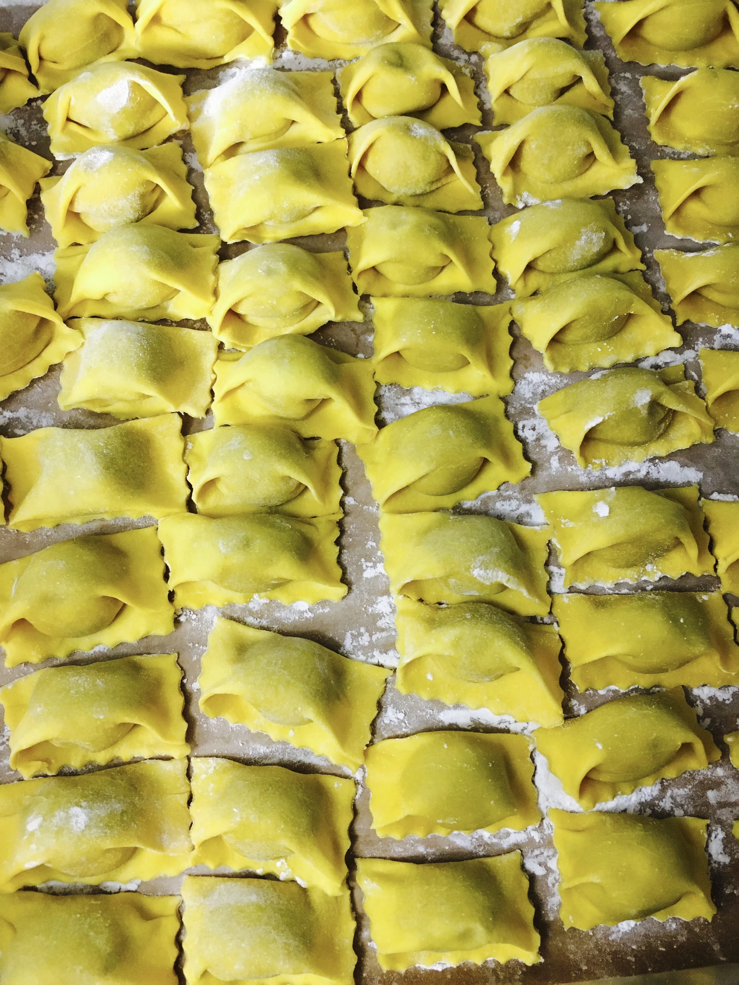 A tray of homemade raw yellow tortellini pasta sprinkled with flour.