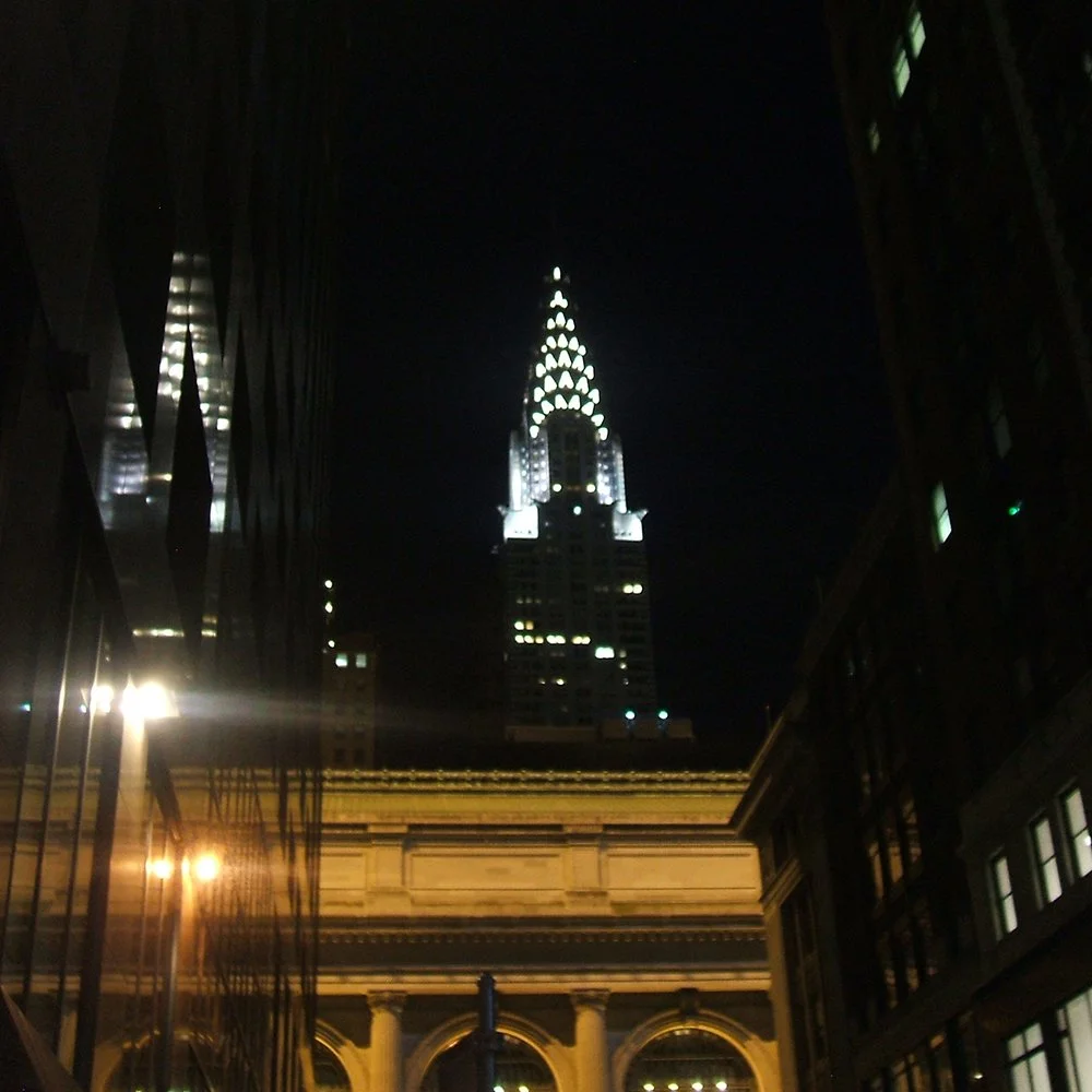 Nighttime cityscape with the illuminated Chrysler Building in New York City, viewed between two tall buildings.