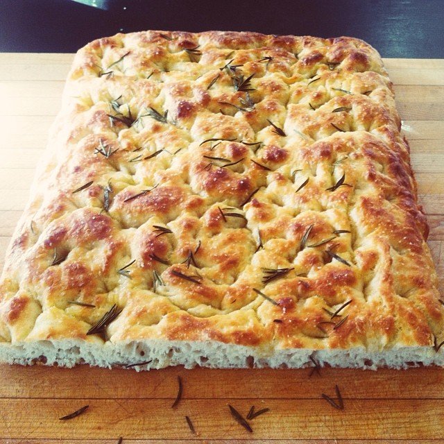 Rectangular focaccia bread topped with rosemary leaves.