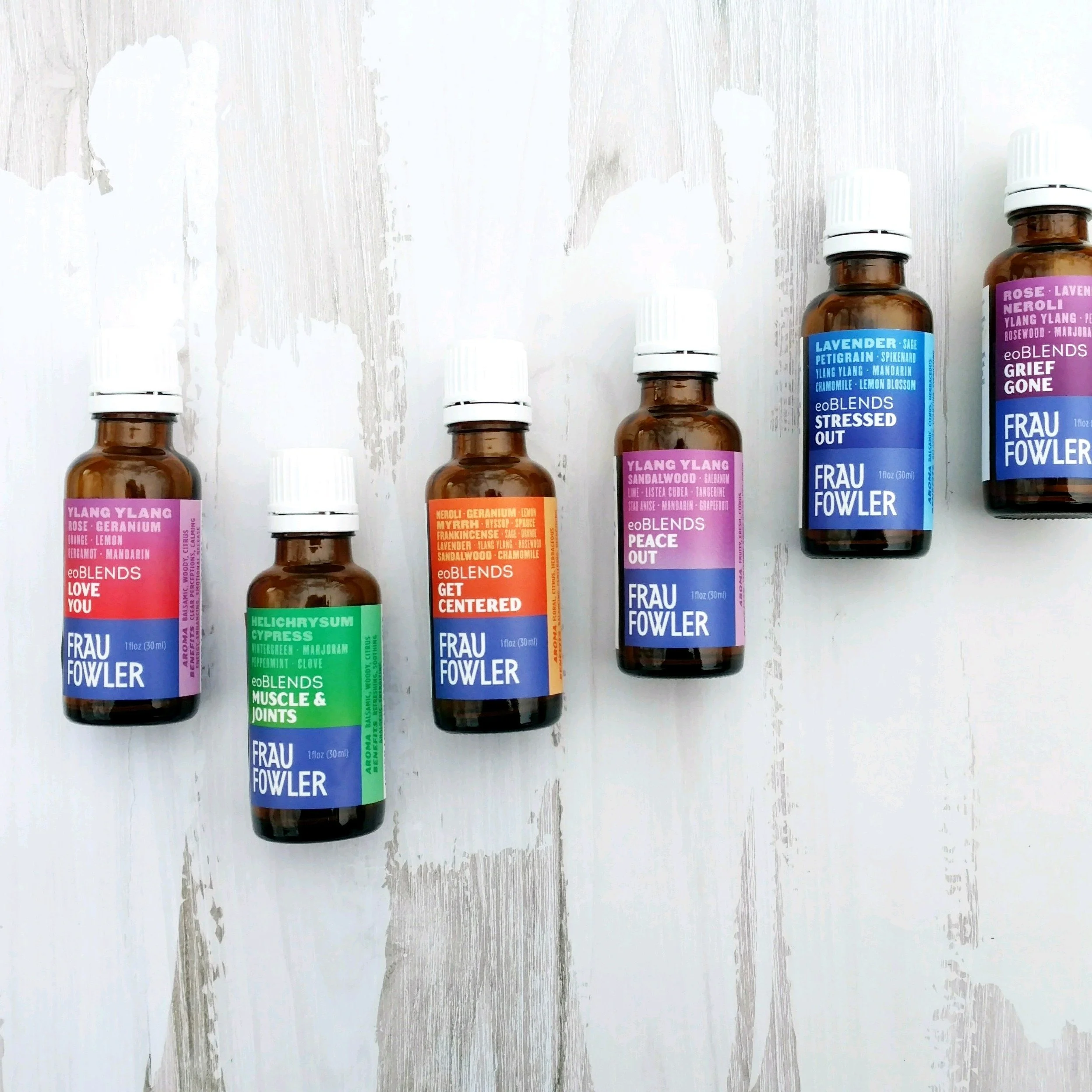 Several small brown glass bottles with white caps, each with colorful labels, placed on a wooden surface with peeling white paint.