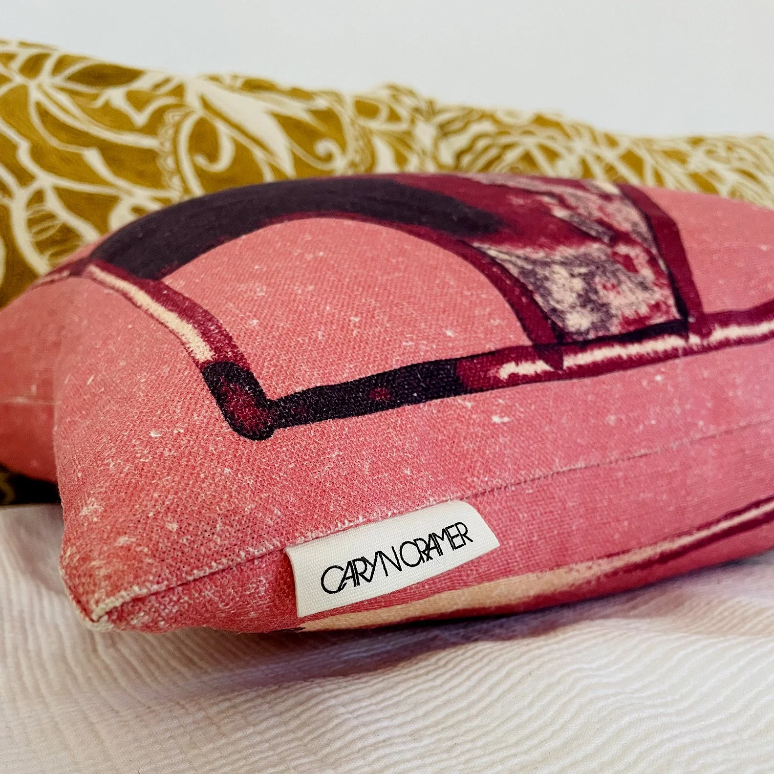 Close-up of a pink fabric item with a black and red graphic design, labeled with the brand name 'CARYNCRAMER' on a white tag.