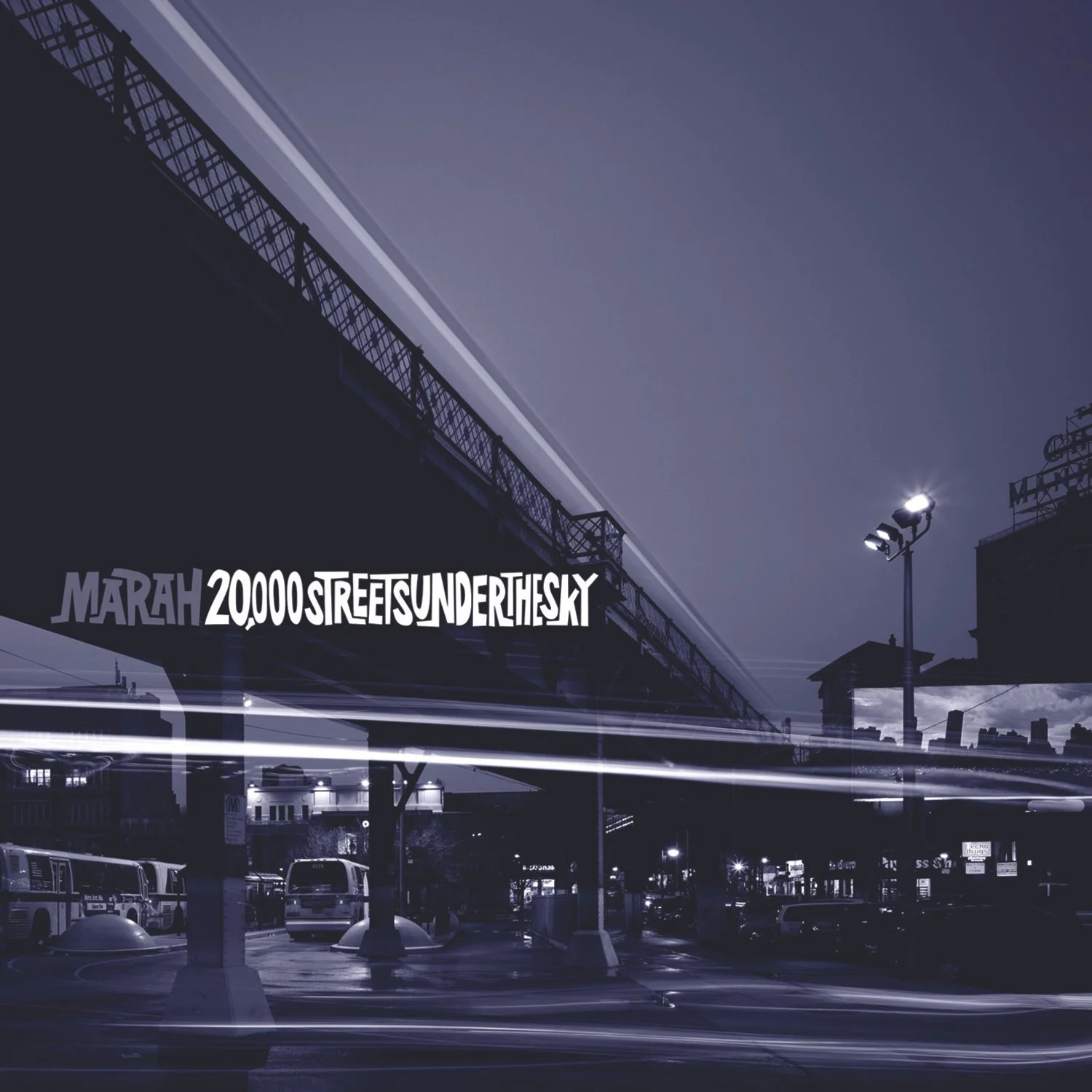 City bus terminal at night with buses parked, a street with streaks of light from passing vehicles, stadium lights, and a bridge overhead, with a building displaying a sign for Mariah 20,000 streams under the sky.