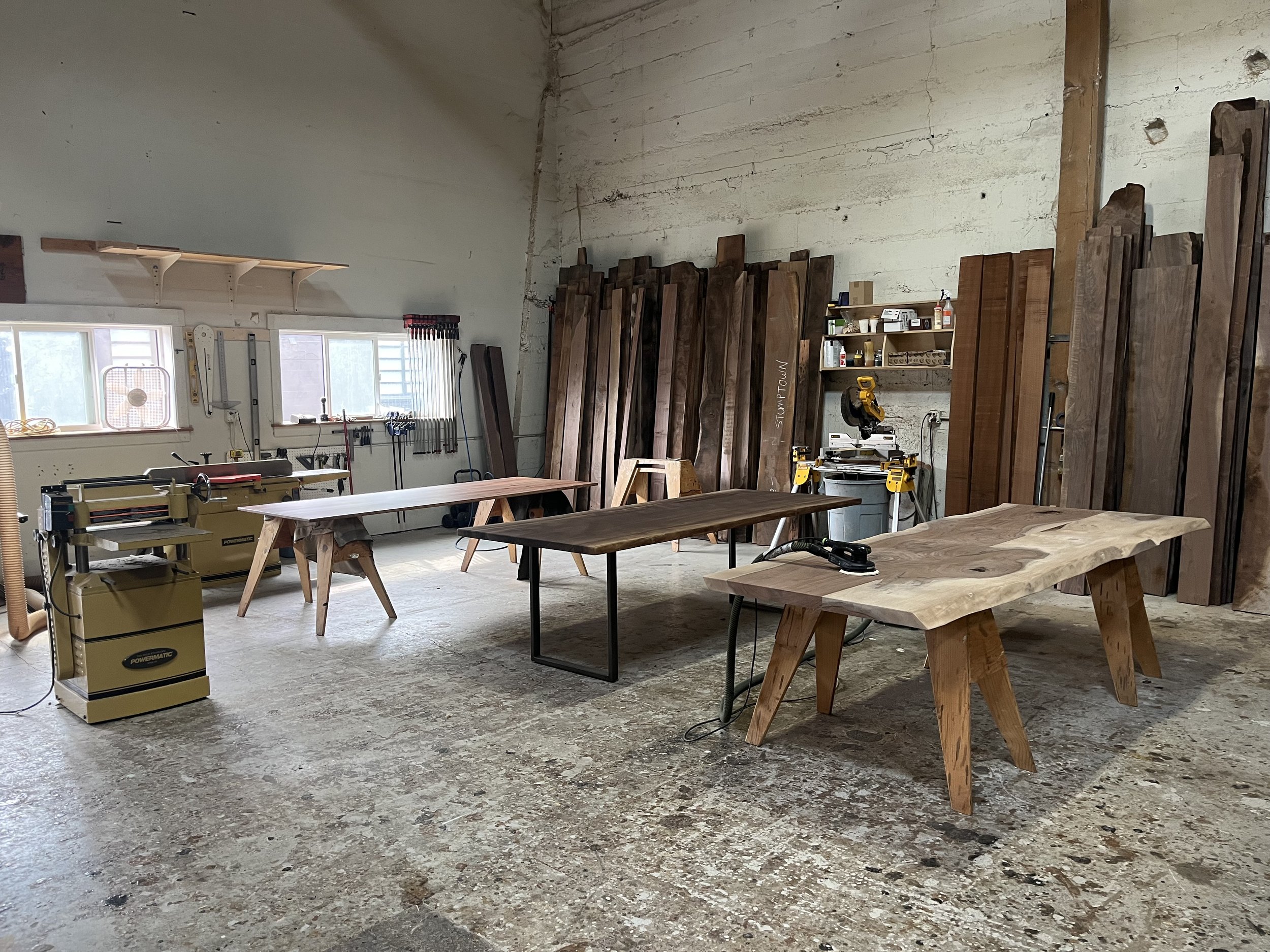 Stumptown Reclaimed wood shop in Portland with walnut slabs on the wall and custom dining tables in progress on sawhorses