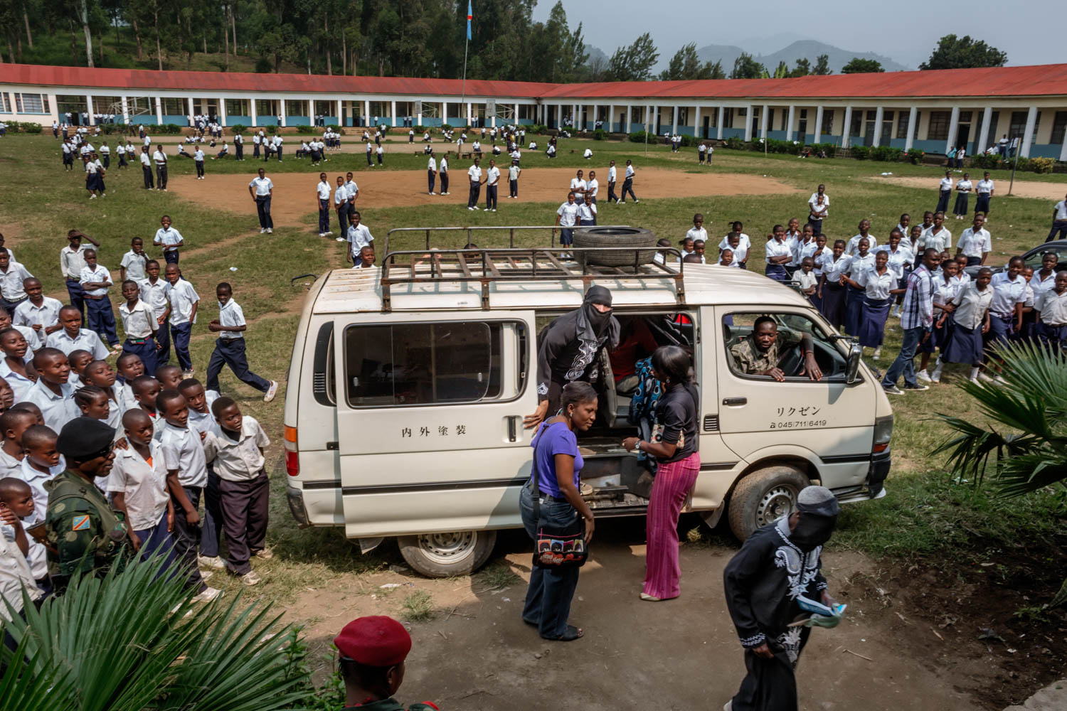   Students flock around a van that is delivering women scheduled to testify. For one week, the trial was held in a makeshift courtroom, set up in the auditorium of a Catholic school in Minova. Since victims could not afford a trip to Goma, more than 