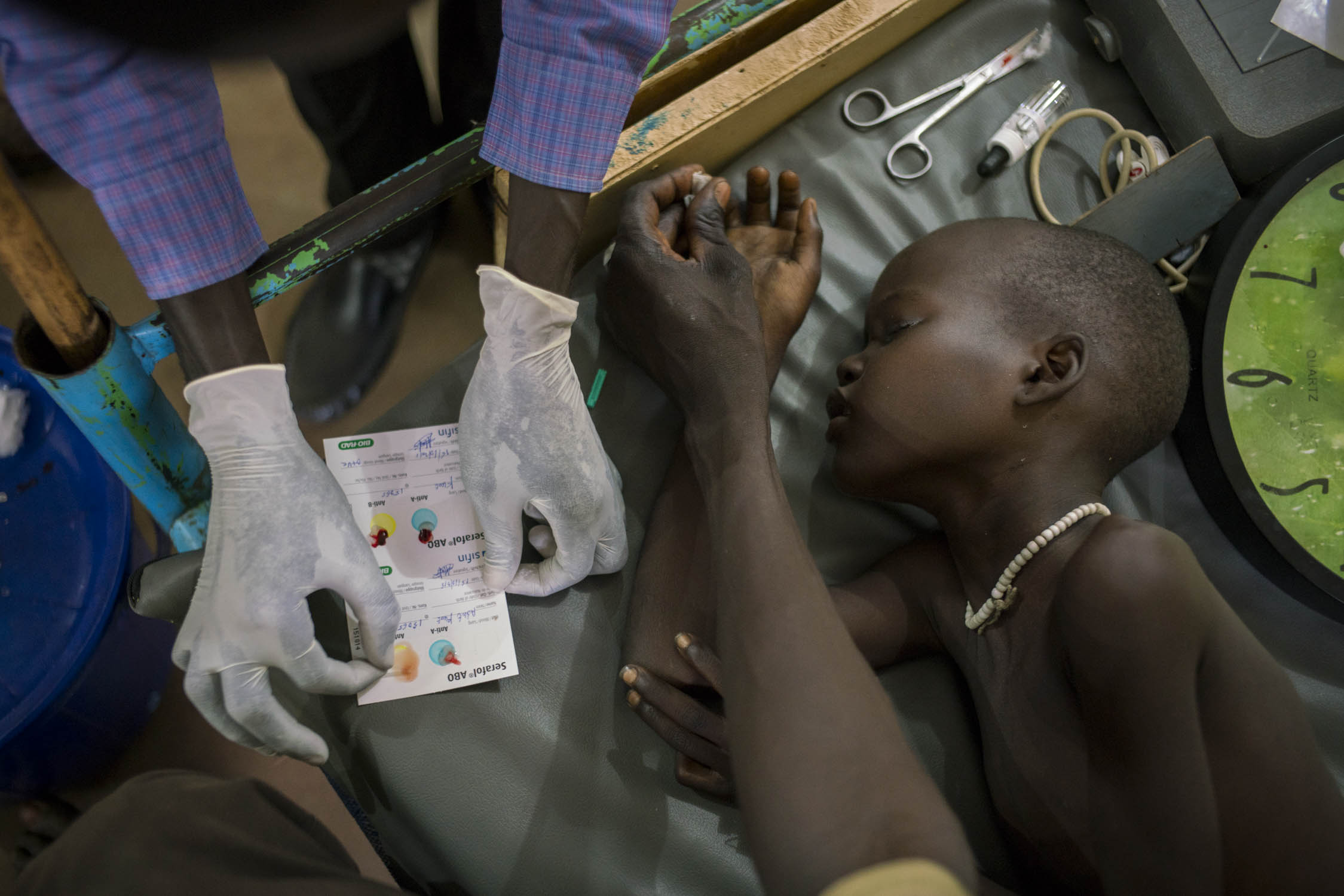  A nurse checks blood-type compatibility before administering a blood transfusion to Adut Chuor Kujal, 8, who is receiving treatment for cerebral malaria at an MSF hospital in Aweil city, South Sudan. Adut's father presses down on her fingertip that 
