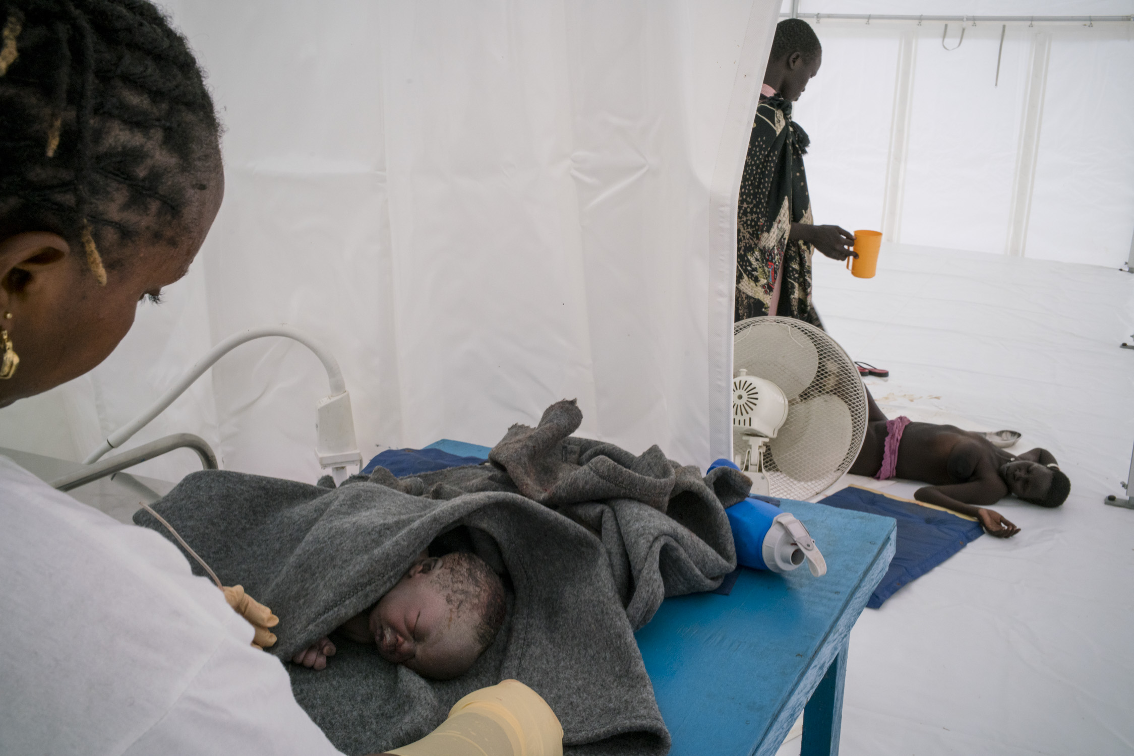  A midwife tends to a newborn who is not breathing or suckling as normally expected, suggesting birth defects,&nbsp;while his mother lies collapsed on the floor of the MSF hospital tent after an extremely difficult delivery. After six children, givin