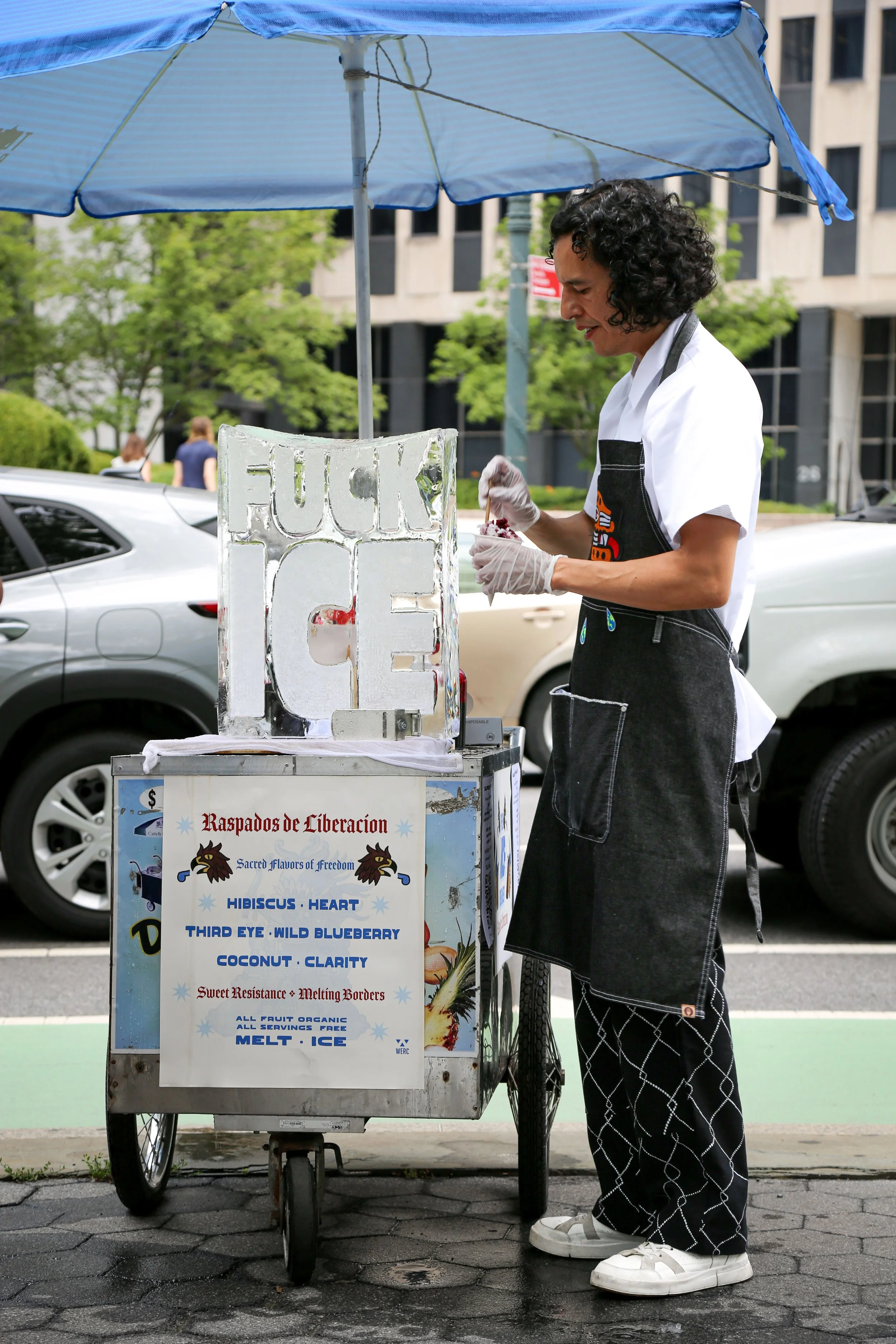 Artist serving raspados from ice block for a ritual offering during Sweet Resistance performance at 26 Federal Plaza, New York City.  2025