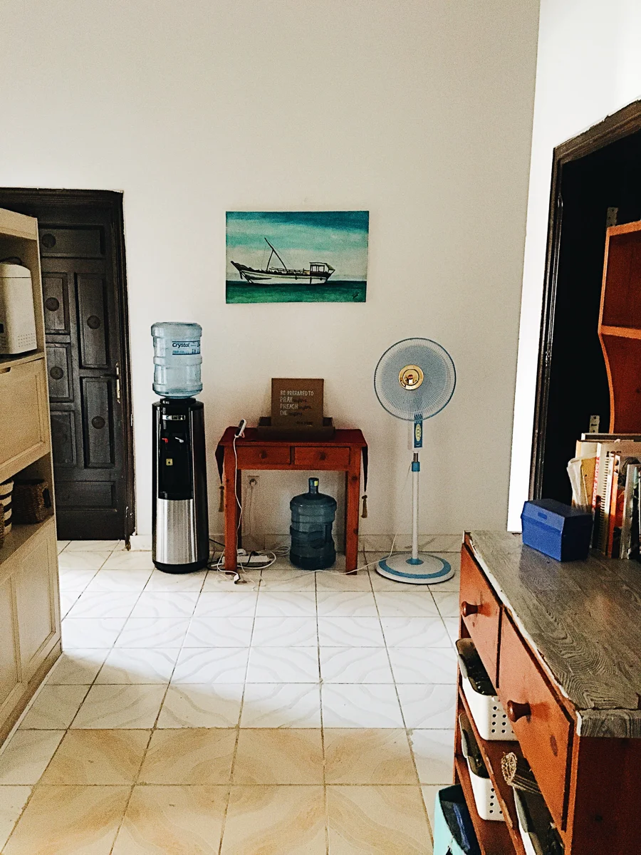 The back of our hallway and to the left is our kitchen. You can see our water tower and after this photo was taken we actually turned that back table into a coffee station. Our coffee collection kept growing and it made since to keep it next to the filtered water. We also had to get a fan for this space because it was the hottest place in the house and where we always ended up talking with visitor forever…equals sooo much sweaty conversations. You can also see the original contact paper of the furniture piece and how much better it looks with new knobs and contact paper, a cheap and easy fix! To the left you can see part of the other piece of furniture we had in this space—holding mostly all of our kitchen appliances.