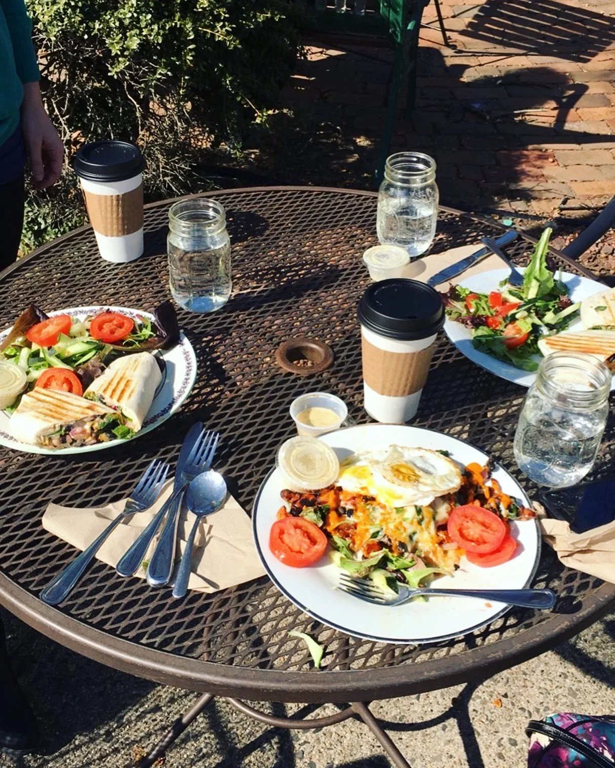  Outdoor cafe table with sandwiches, salads, coffee, and water at BeWell Bakery &amp; Cafe. 
