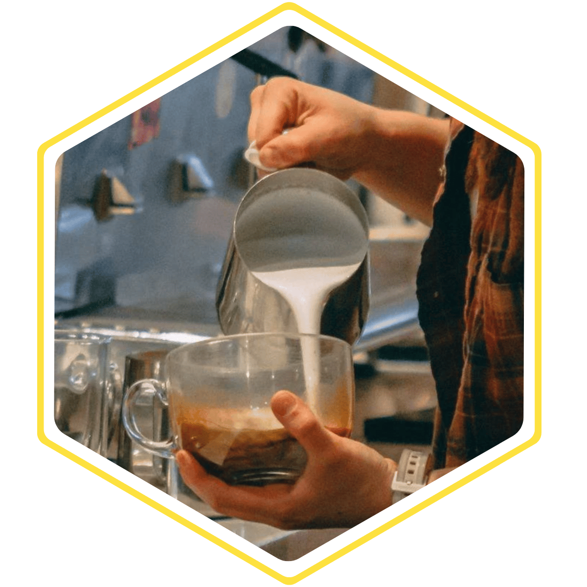Barista pouring steamed milk into a glass mug of espresso at BeWell Bakery & Cafe.
