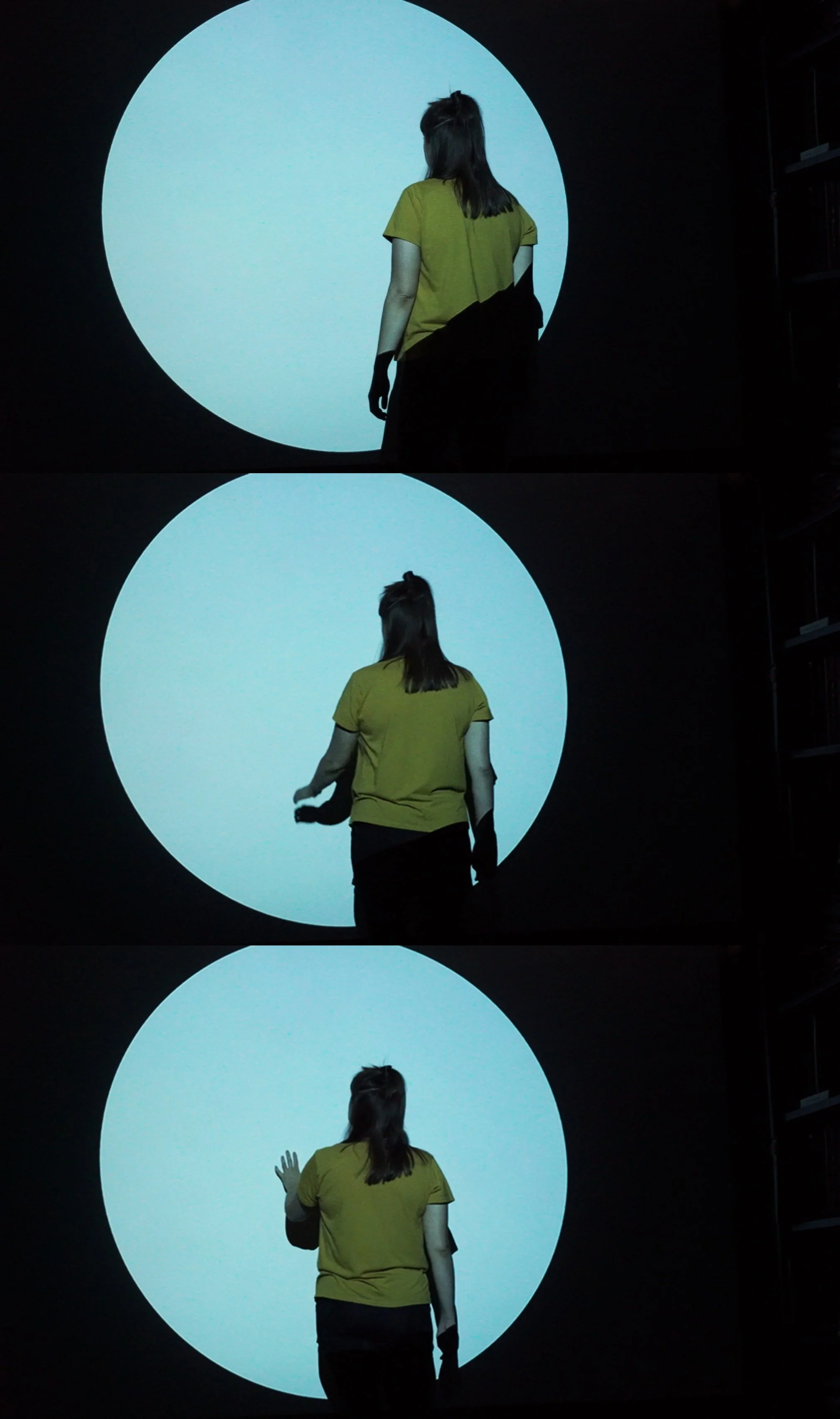 set of 3 film still images of a digital video projection of large blue circle in a dark room with a woman standing close to the circle creating a silhouette in the image
