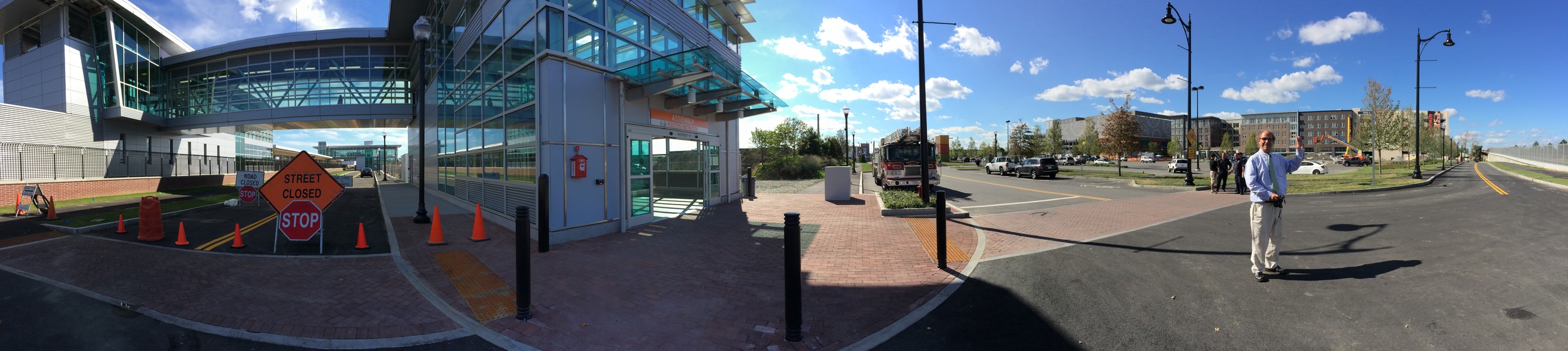 A panorama of the area awaiting development around the unfinished Assembly station entrance with Wig Zamore of the MBTA Rider Oversight Committee and chair of the Union Square Civic Advisory Committee .