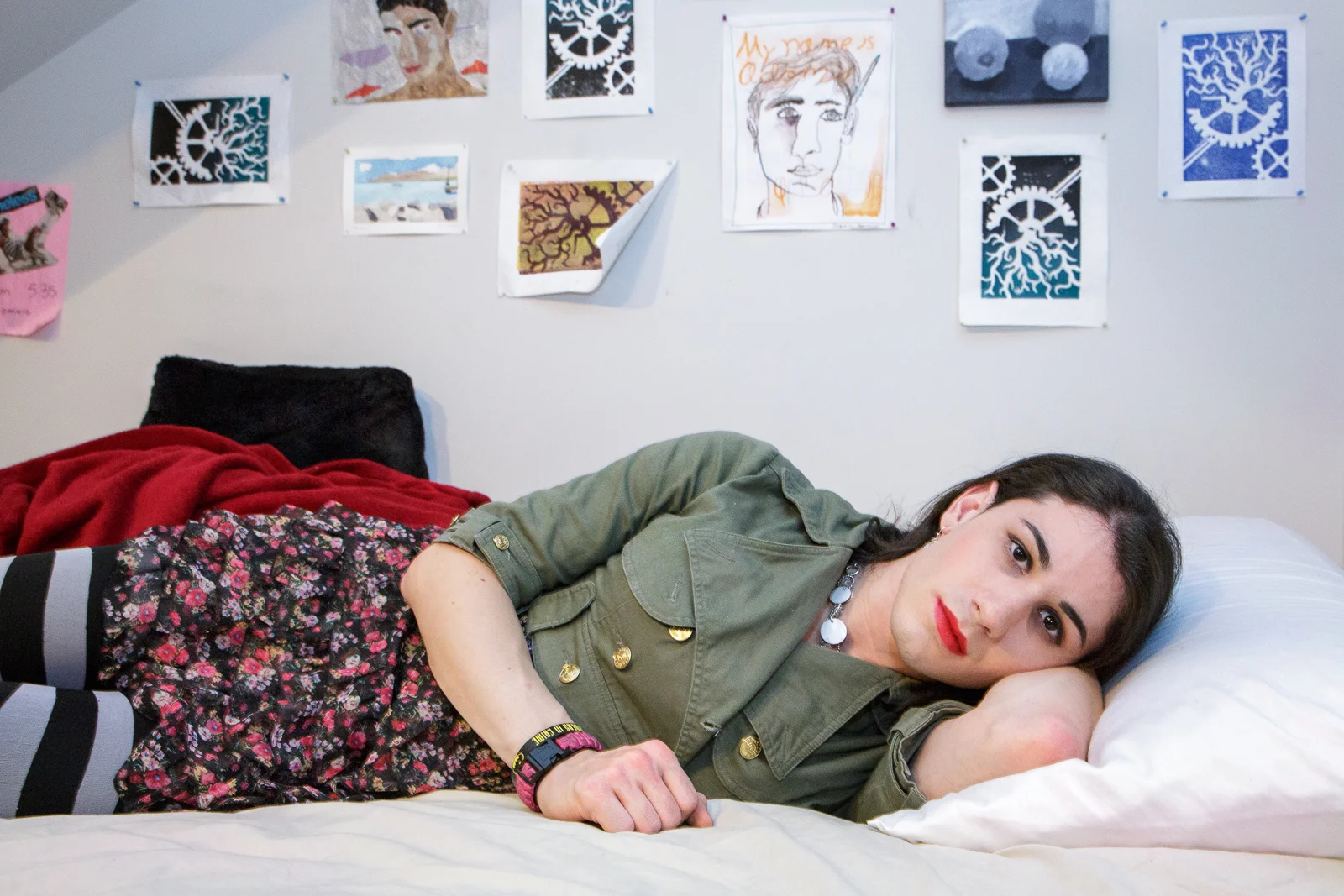 Ashley lies on her bed, in front of drawings she made as a young boy.