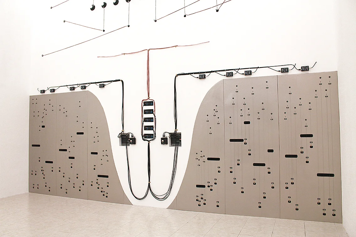 The lower part of the wall is made out of wood and holds sixty piano strings on it. The space between this new wall and the former wall acts as a sound box, the vibration of the strings are picked up by contact microphones placed in the sound box.