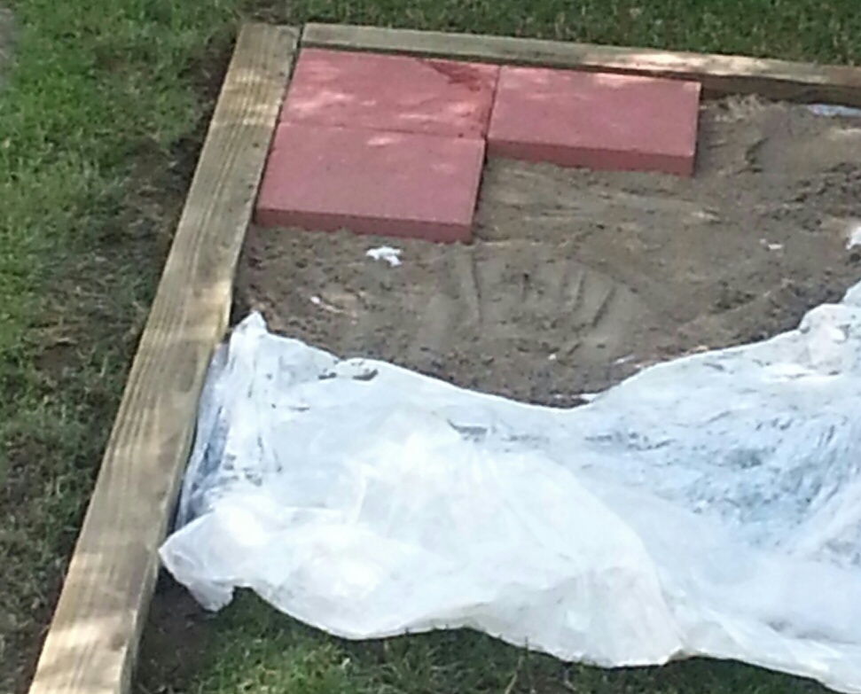 Plastic was layed on the ground to kill the grass underneath to prevent it from growing up between the blocks, and then a layer of sand to set the 12" x 12" pavers in. (We found the best price for the pavers at Home Depot.) It took some time to make the corners meet and make them level but we all know anything doing is worth doing right.