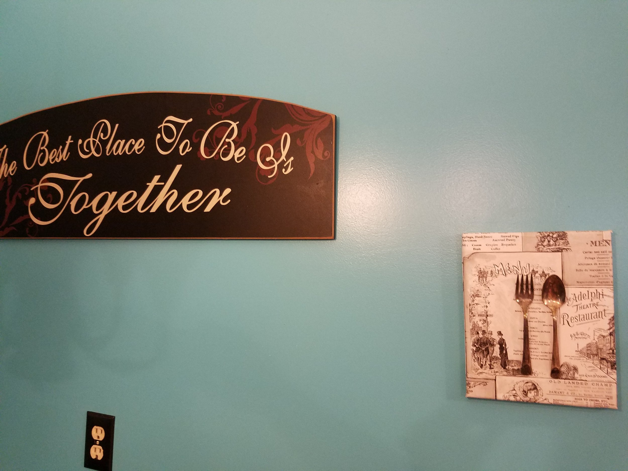 Taking a cue from the existing Fork and Spoon graphic art, a solution was needed to cover an old wall phone jack. Here, a canvas was covered in wallpaper, then a vintage tarnished utensils were adhered.