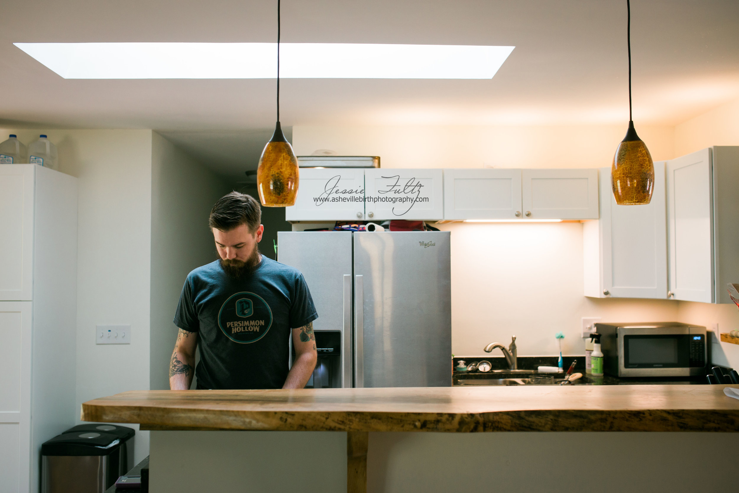 man in black t-shirt standing behind wooden-top bar in kitchen