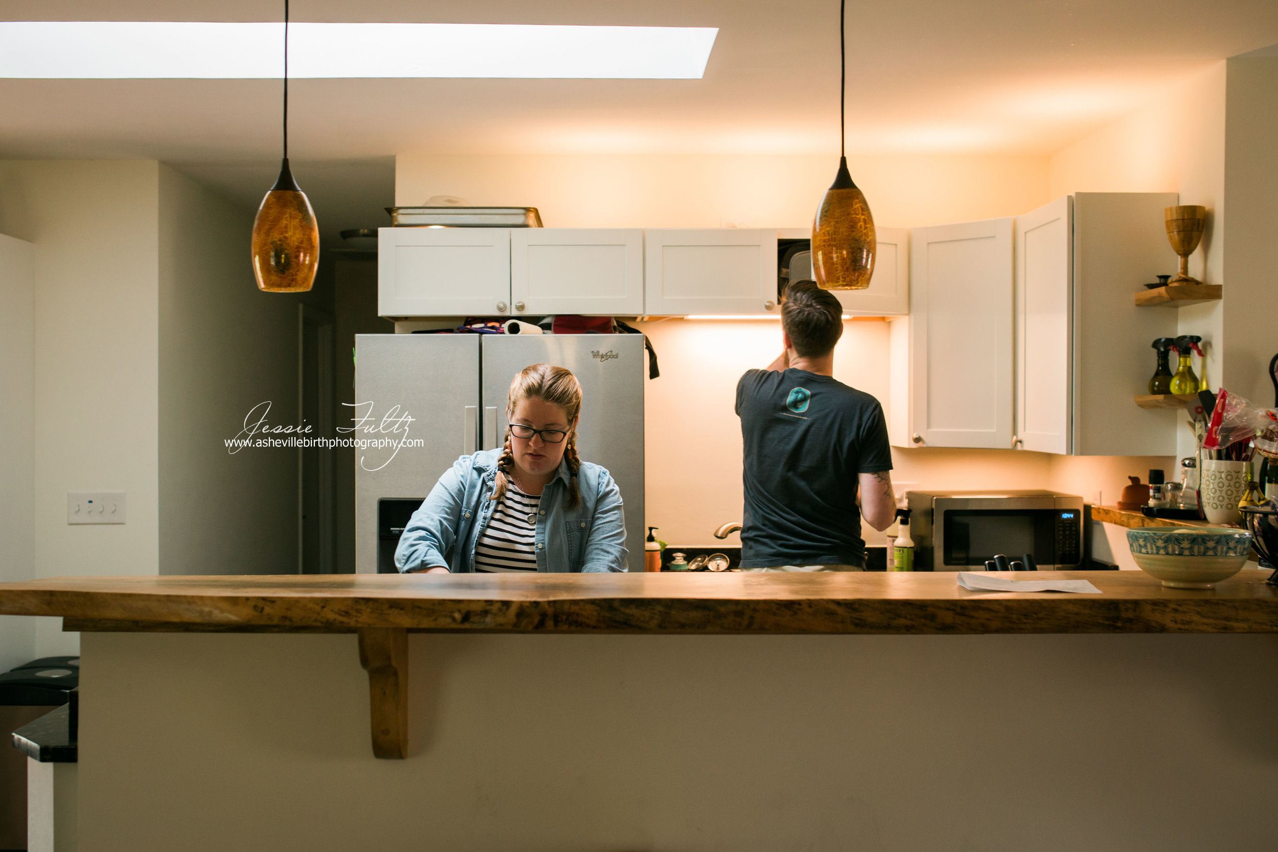 pregnant woman with pigtail braids standin behind wooden-top kitchen bar