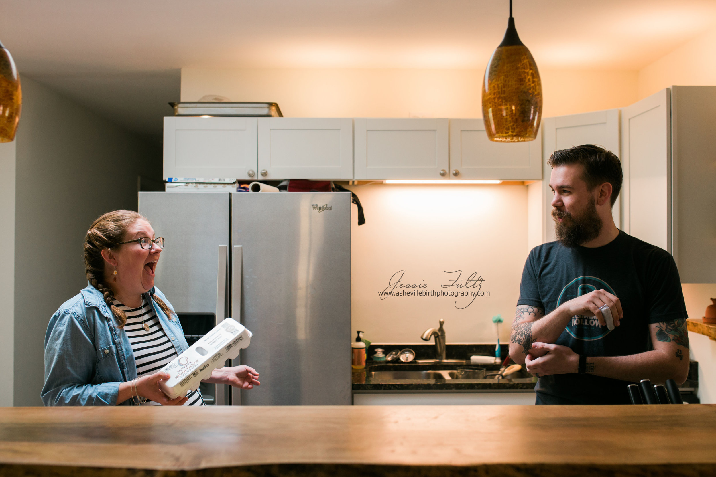 husband and wife standing behind their wooden-top kitchen bar laughing at each other while woman holds a carton of eggs