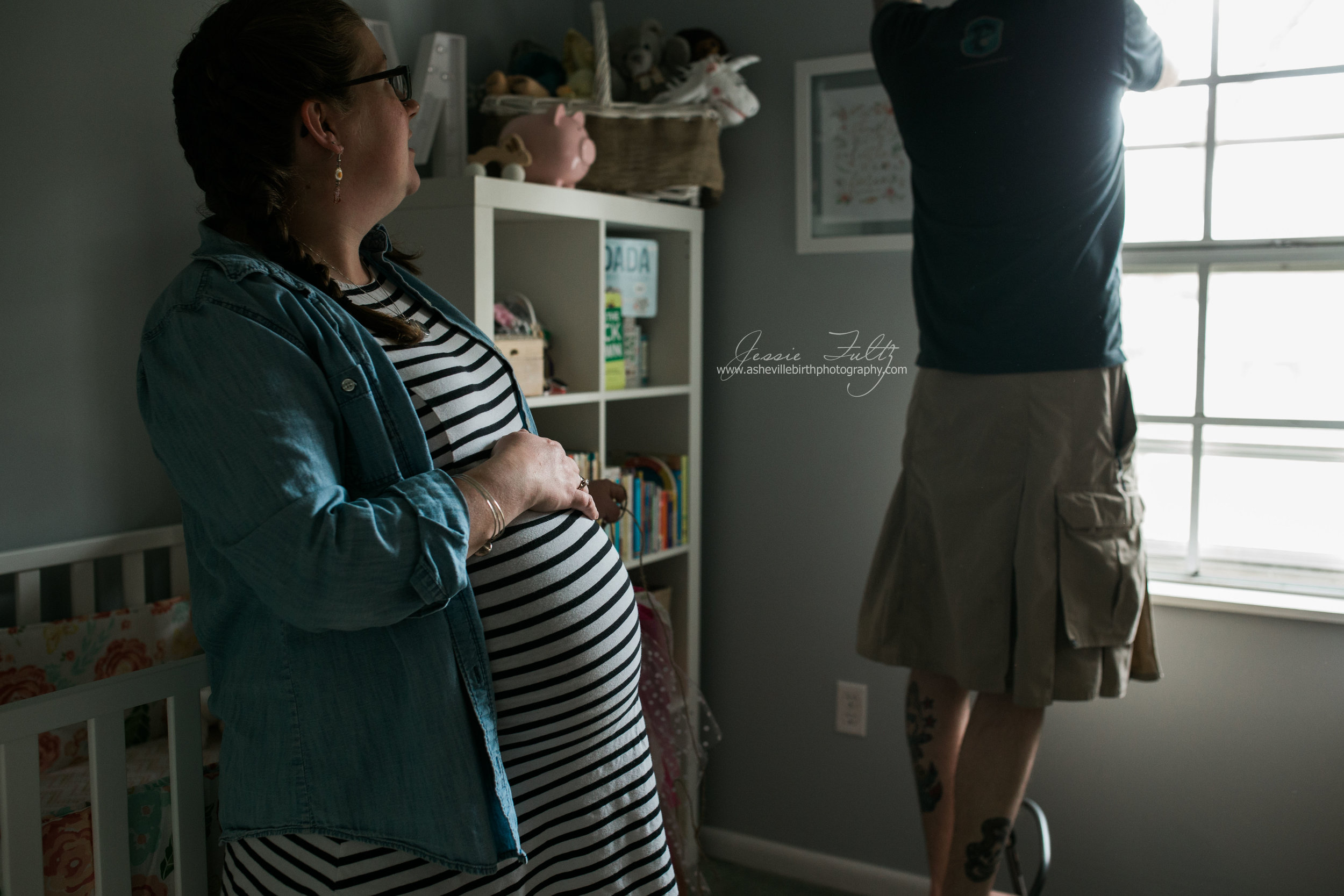profile of a pregnant woman in a striped dress holding her belly and leaning on her baby's crib