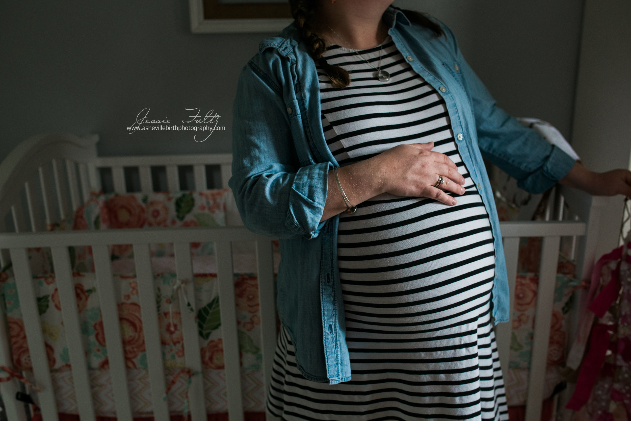 pregnant woman in striped dress holding her belly and leaning on her baby's crib