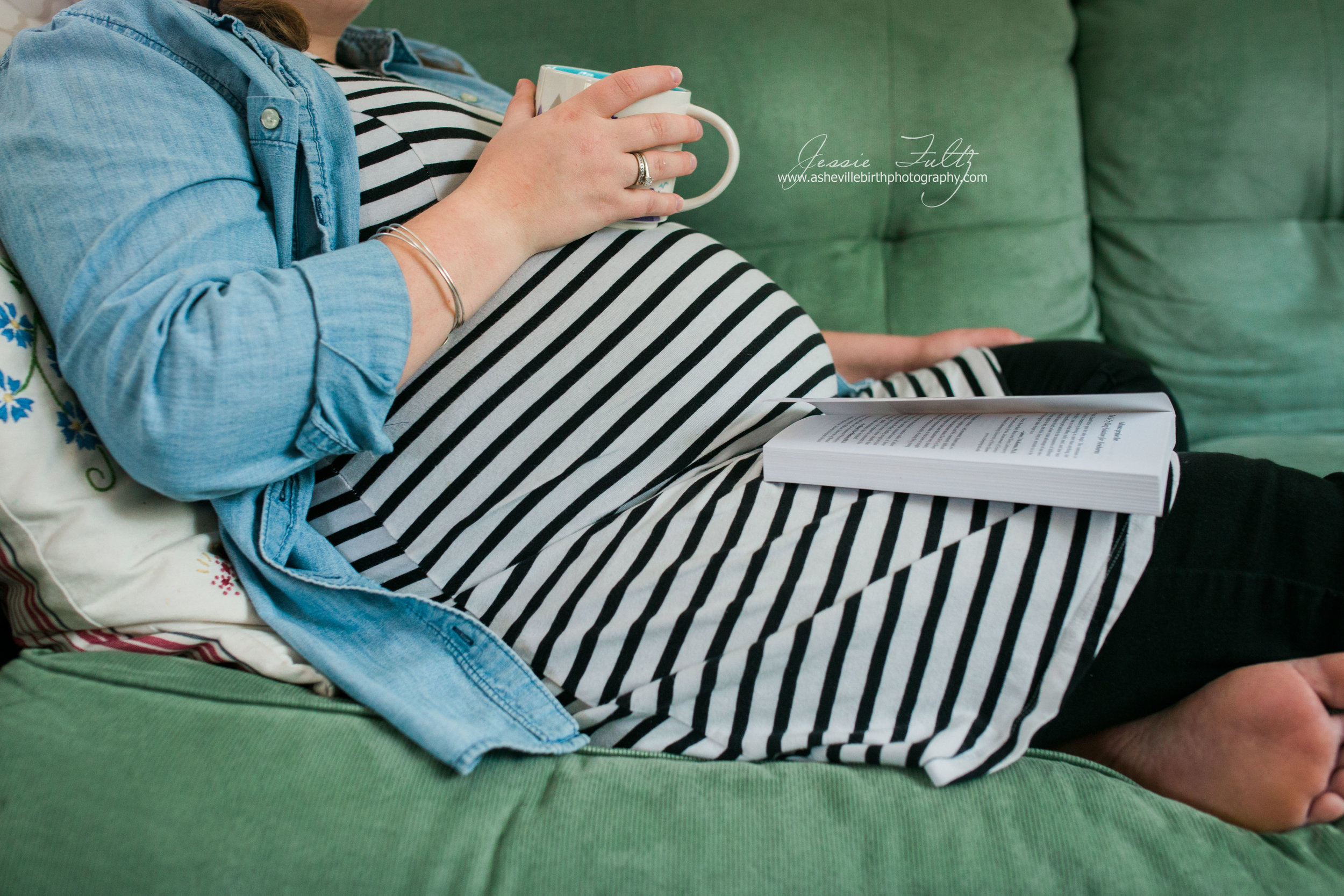 close-up picture of a pregnant woman in a striped dressresting her coffee mug on her belly and a book in her lap
