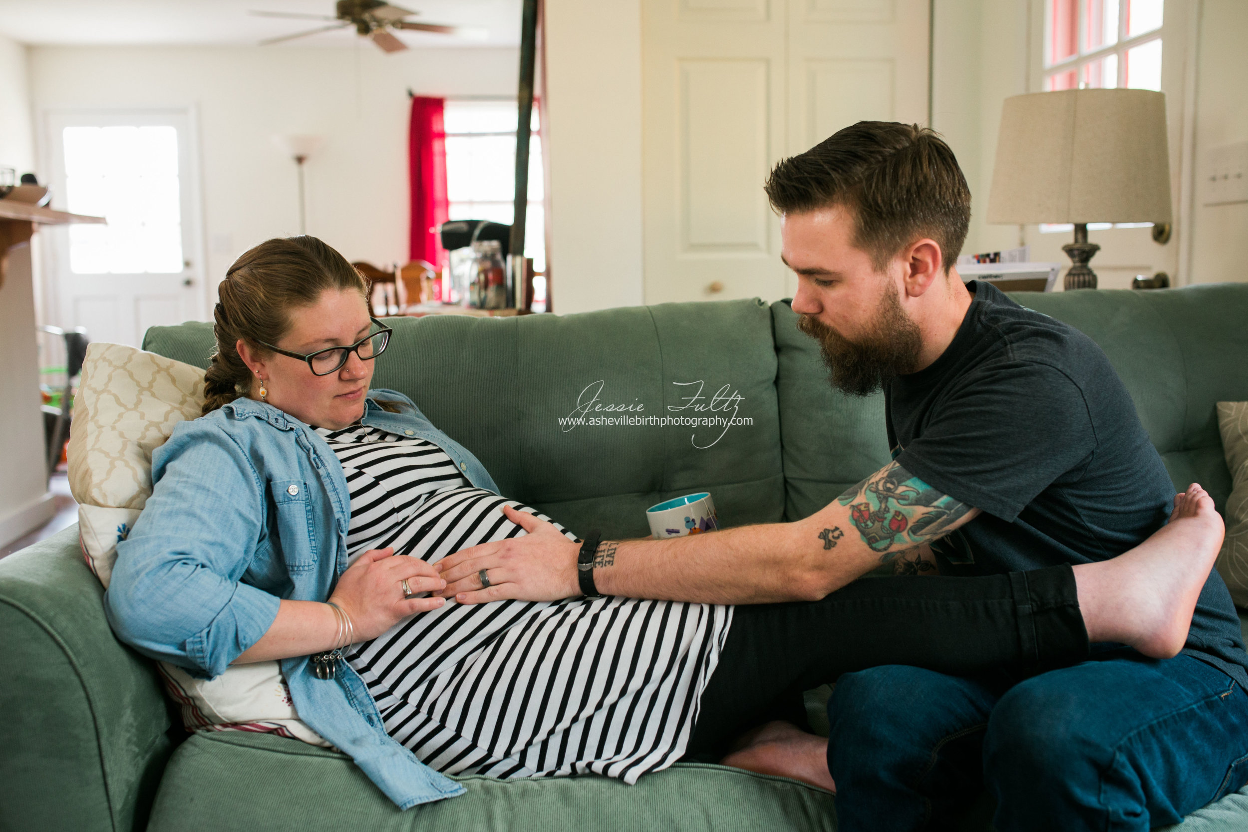 a pregnant woman and her husband sitting on the couch and feeling the baby kick