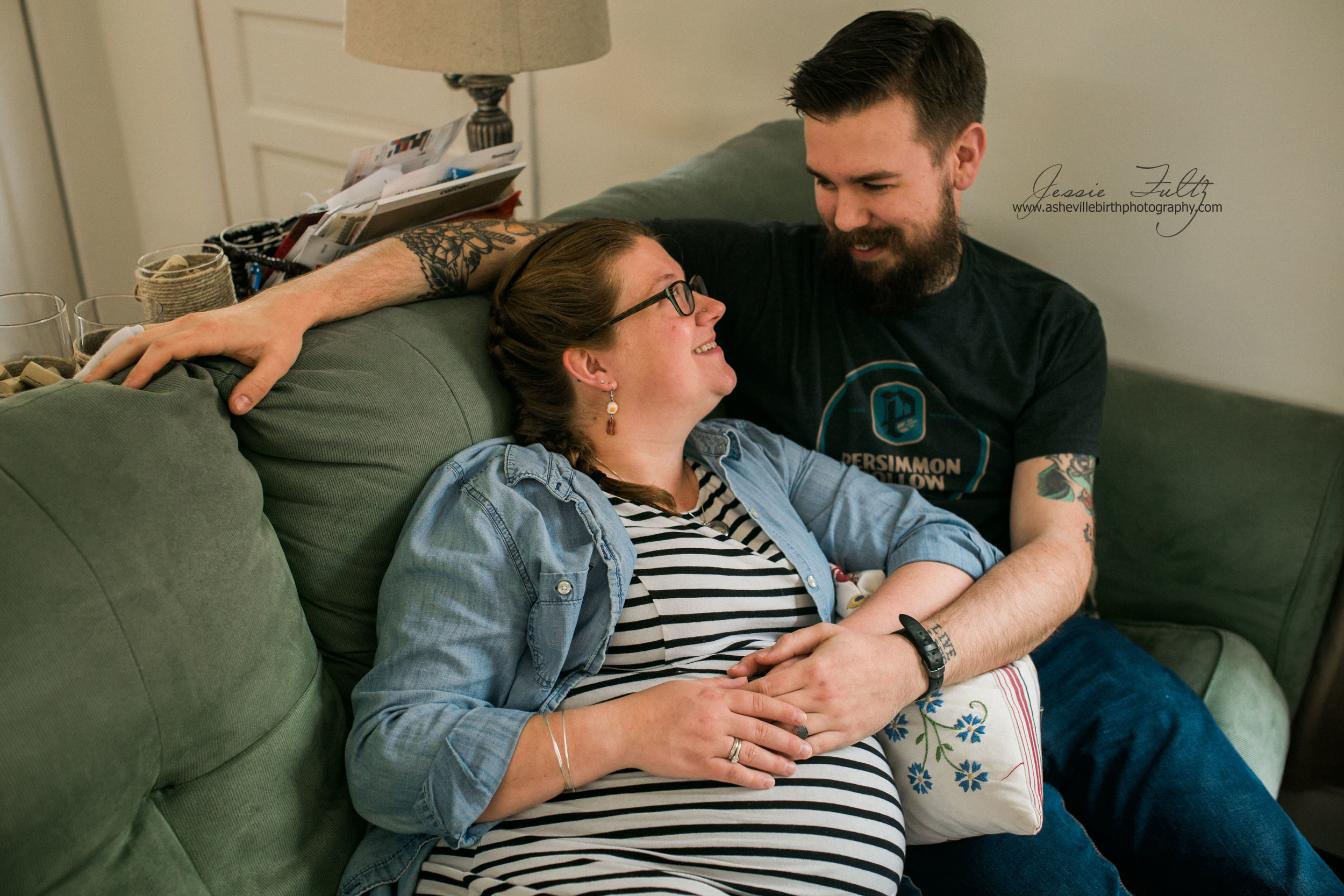 pregnant woman in striped dress and husband cuddling up on the couch and laughing