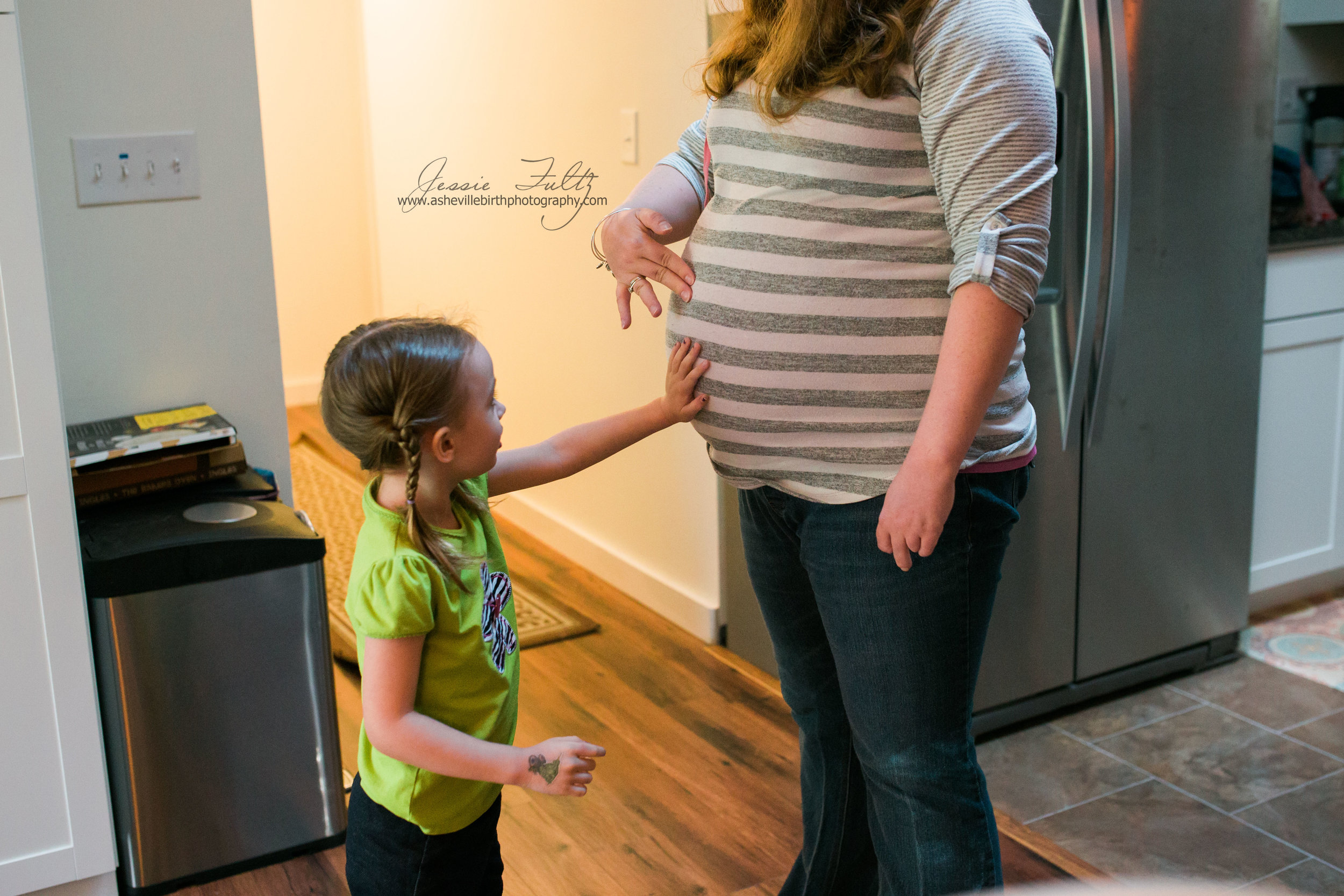 a young girl in a green shirt and pigtails touching a pregnant woman's belly