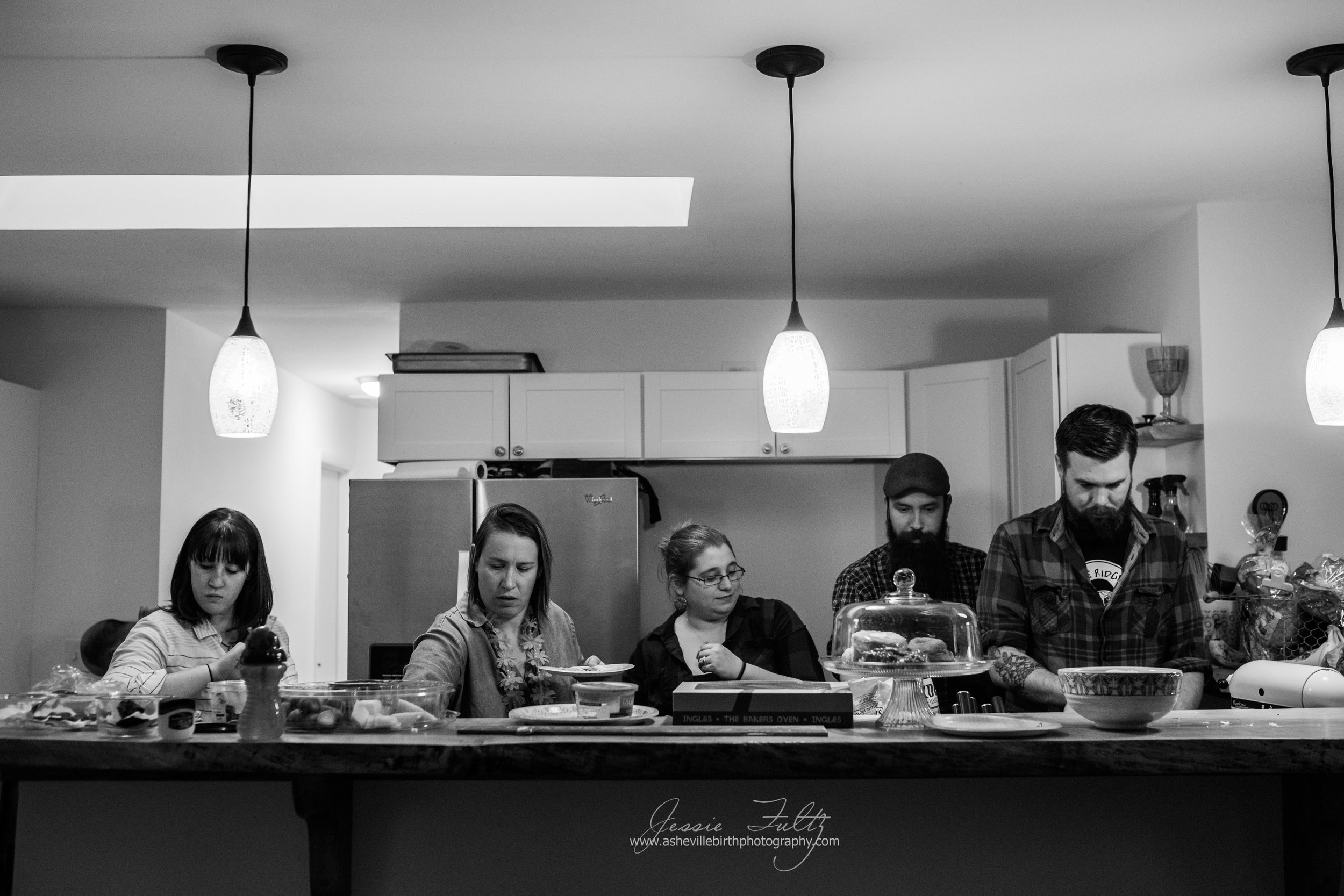 a wide-angle black and white picture fo a group of friends standing behind a kitchen bar