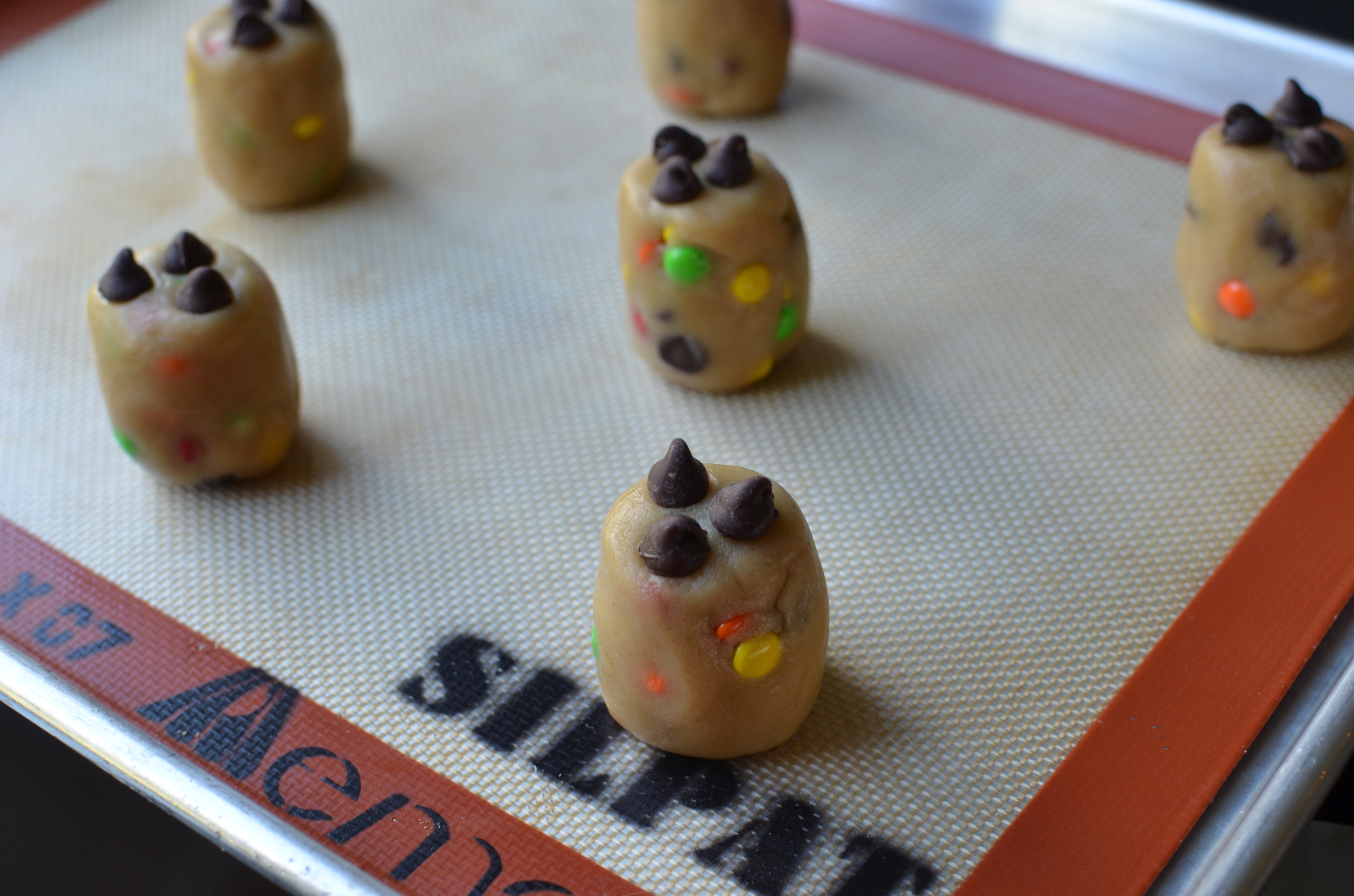 Then shape each of the dough balls into a barrel shape - they should be a bit taller than they are wide. Place 3 chocolate chips on top of each (not necessary, but doing so will look nice then the cookies are done). Place on prepared sheet pans; bake and cool as directed.