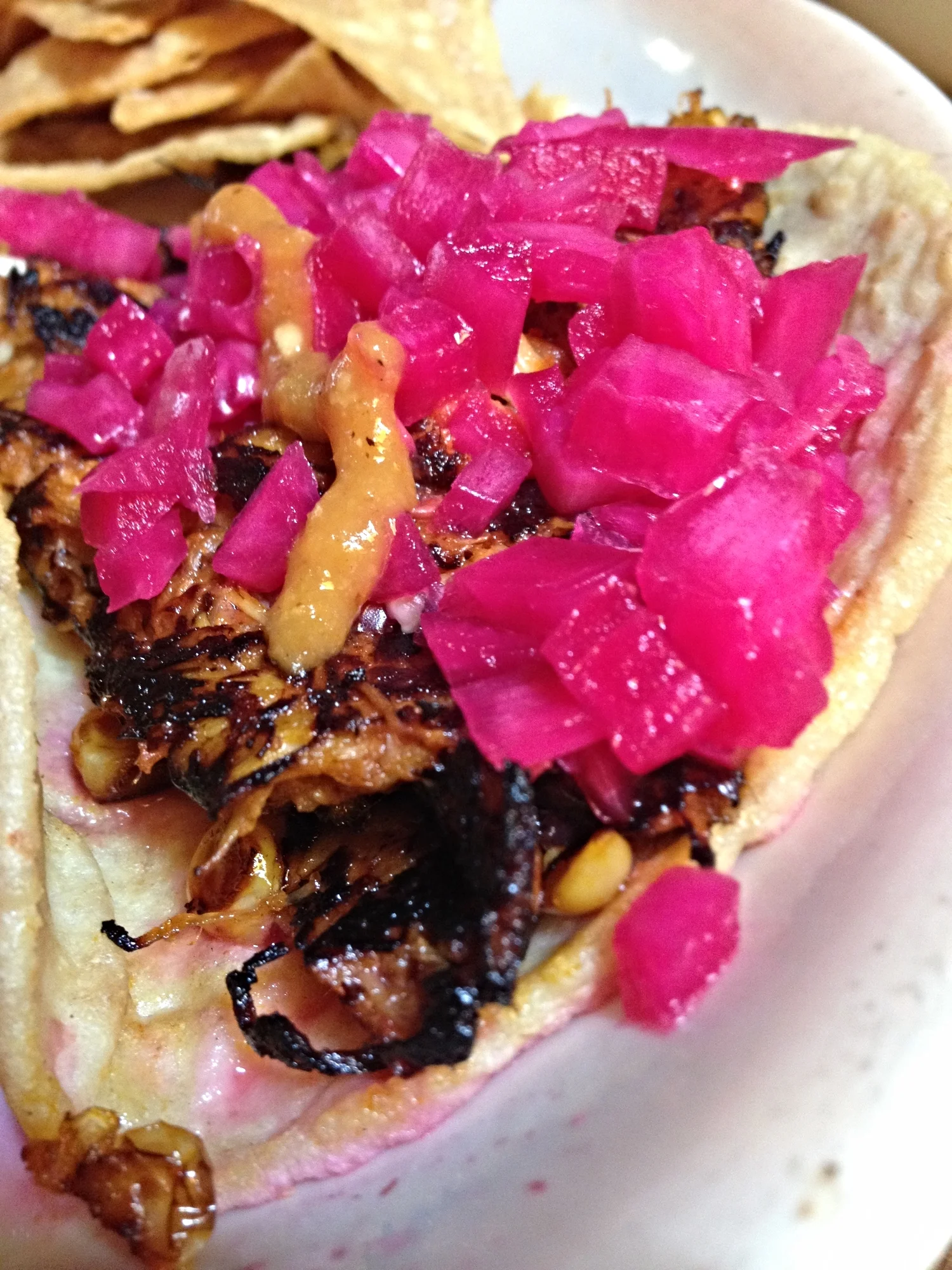 Cochinita Pibil taco with long braised banana-leaf wrapped pork marinated with bitter and sweet orange, rubbed with achiote, grilled on a plancha, and adorned with pickled onions and habanero salsa