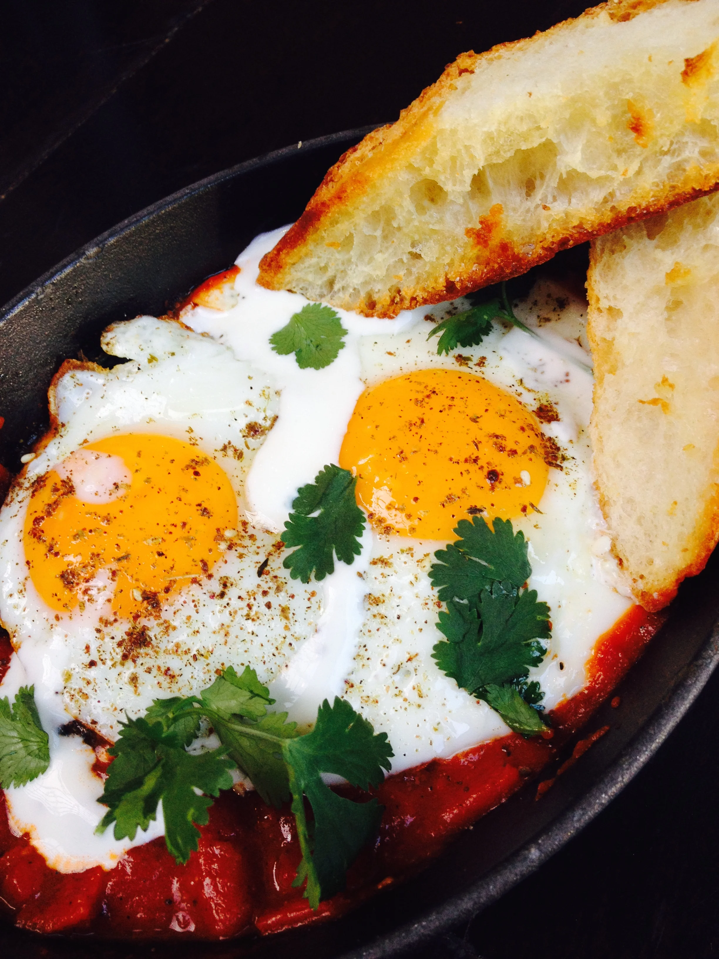 Shakshouka, a Middle Eastern breakfast dish of eggs in a sauce of tomatoes, onions, and cumin, served with grilled bread.